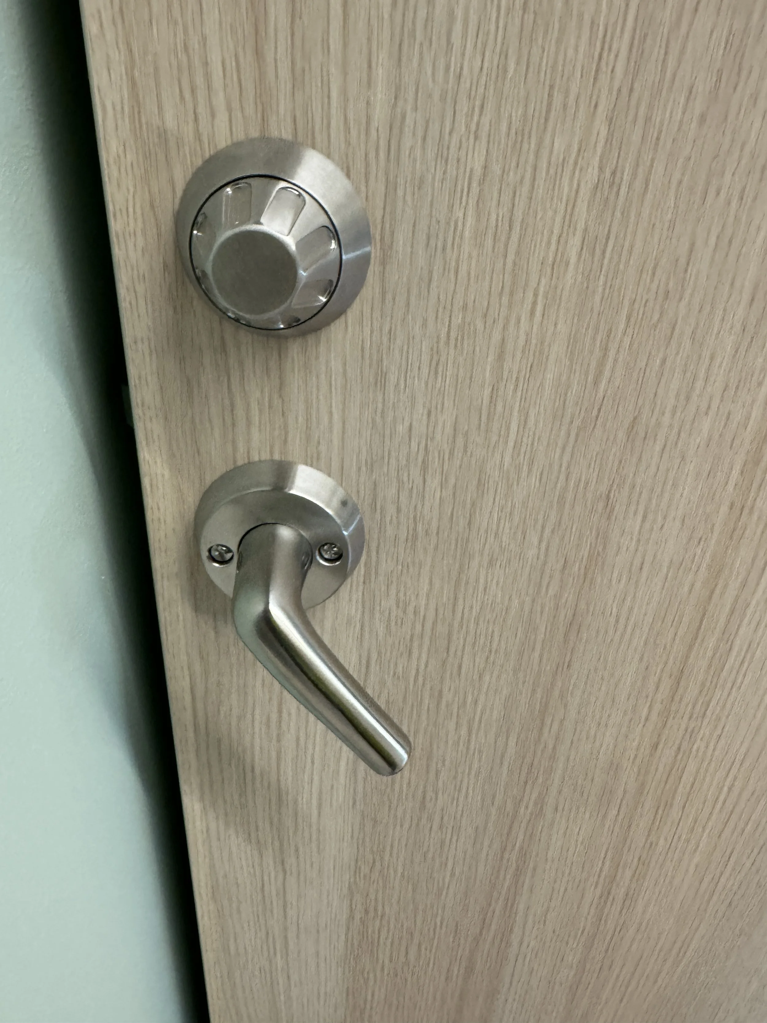 Låse på en lysegrå, tre- eller finer- overflater. To runde metallknapper, en nær toppen og en nær midten med håndtak, den nederste fungerer som dørhåndtak.
