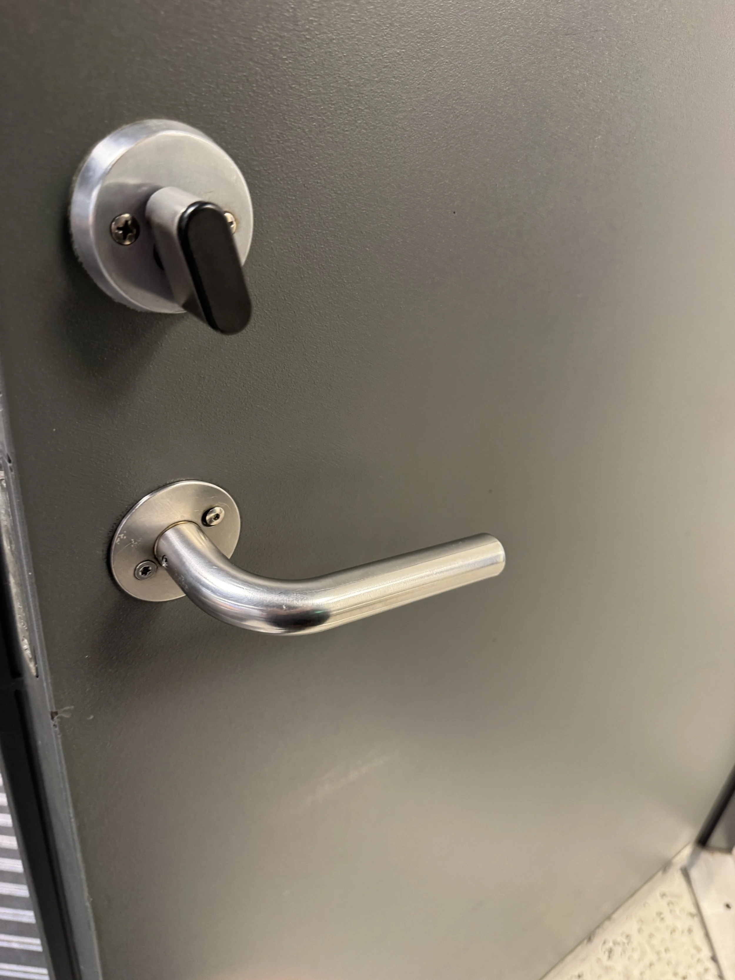 Nærbilde av en dørlås med en svart nøkkel og et dørhåndtak i metall på en grå dør.