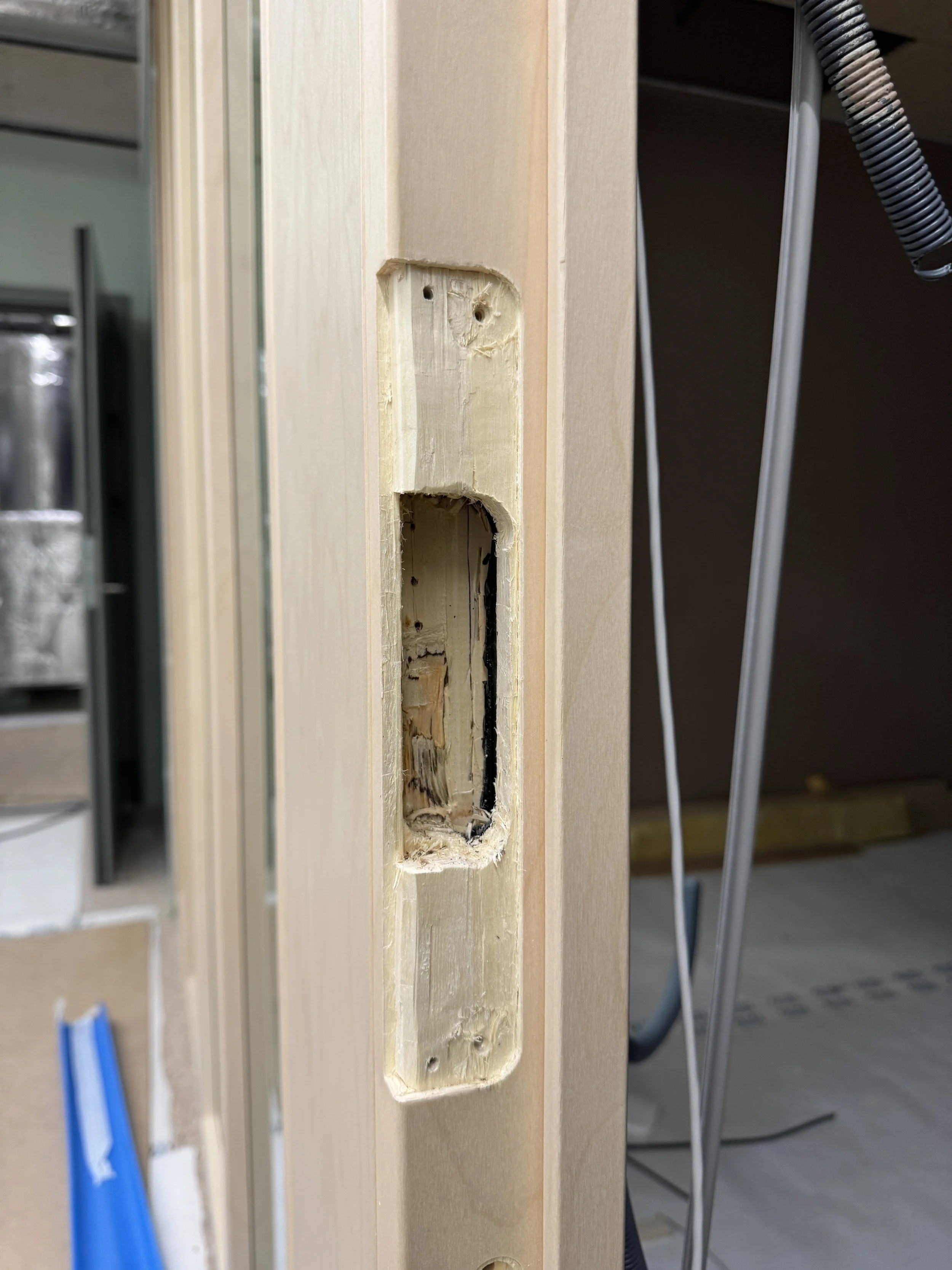 Nærbilde av en treplate med et utgravd hull, sannsynligvis for en dørhåndtak eller lås. Det er synlige skruer og treverker.