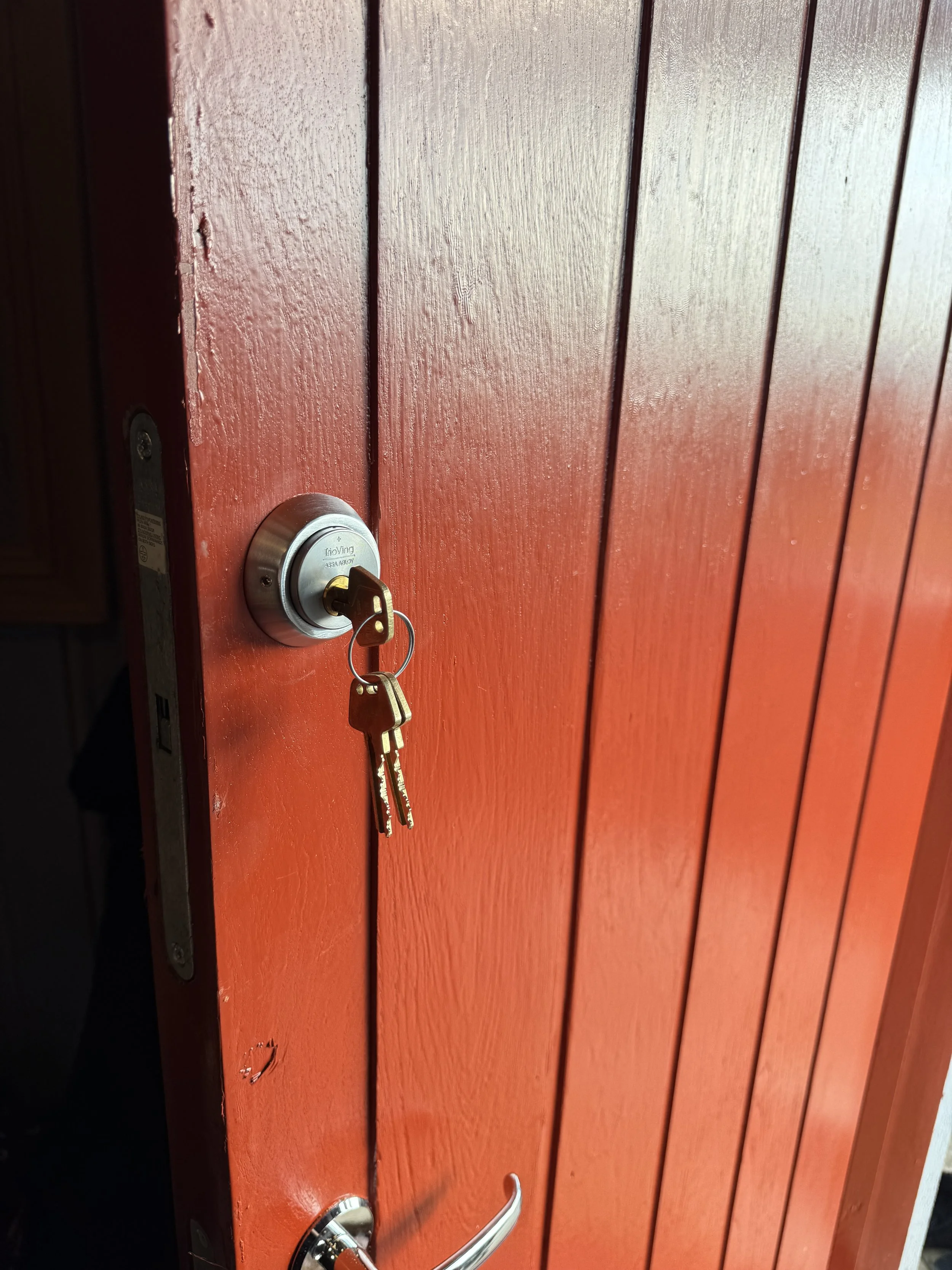 En rød utvendig dør med dørhåndtak og nøkkel i låsen.