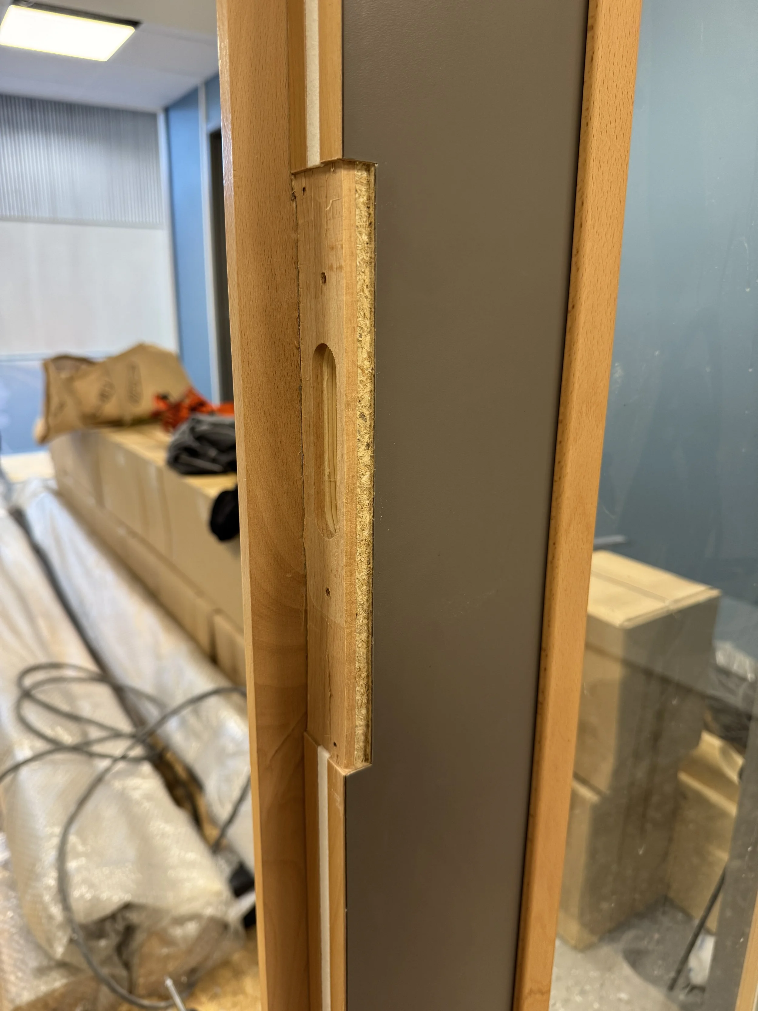 Nærbilde av en trekonstruksjon med en skive, under oppsetting av en vegg. Bakgrunn med utstyr og møbler under konstruksjonsarbeid.