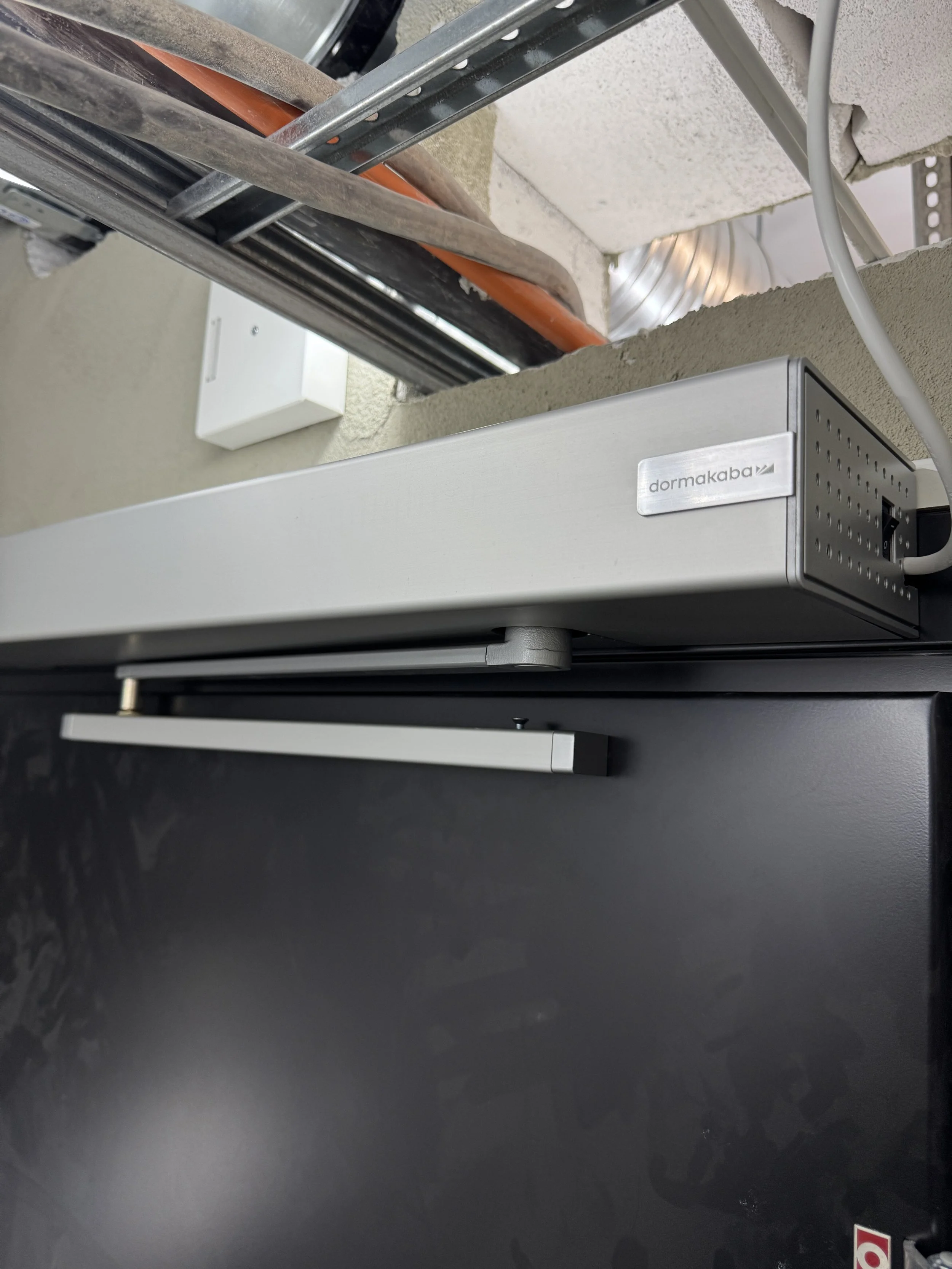 Nærbilde av et lite kjøleskap eller fryseskap, med en metallklokke eller vekt på toppen og noen bygge- eller installasjonsverktøy i bakgrunnen.