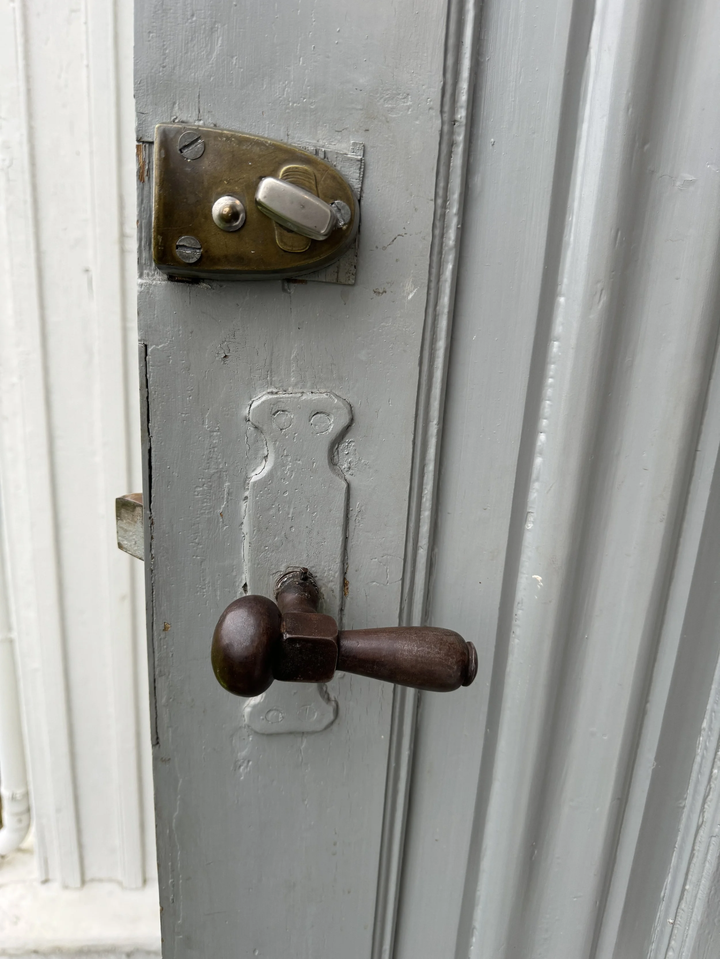 Et gammelt dørhåndtak og en lås montert på en hvit malt treflate på døren.