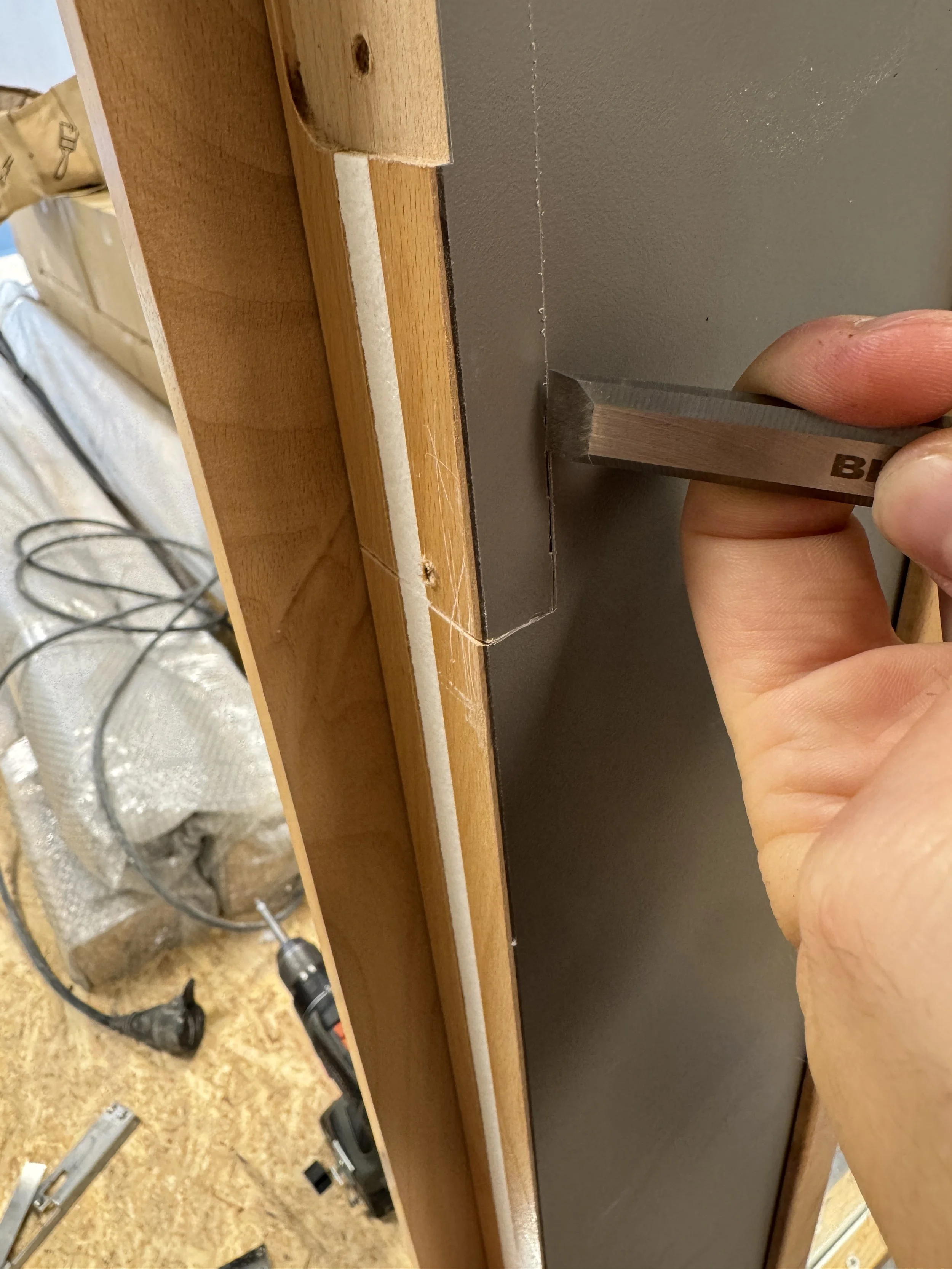 Hånd som bruker en flat skrutrekker til å banke på en vegg med furu- og MDF-plate i en treverkstøtte.