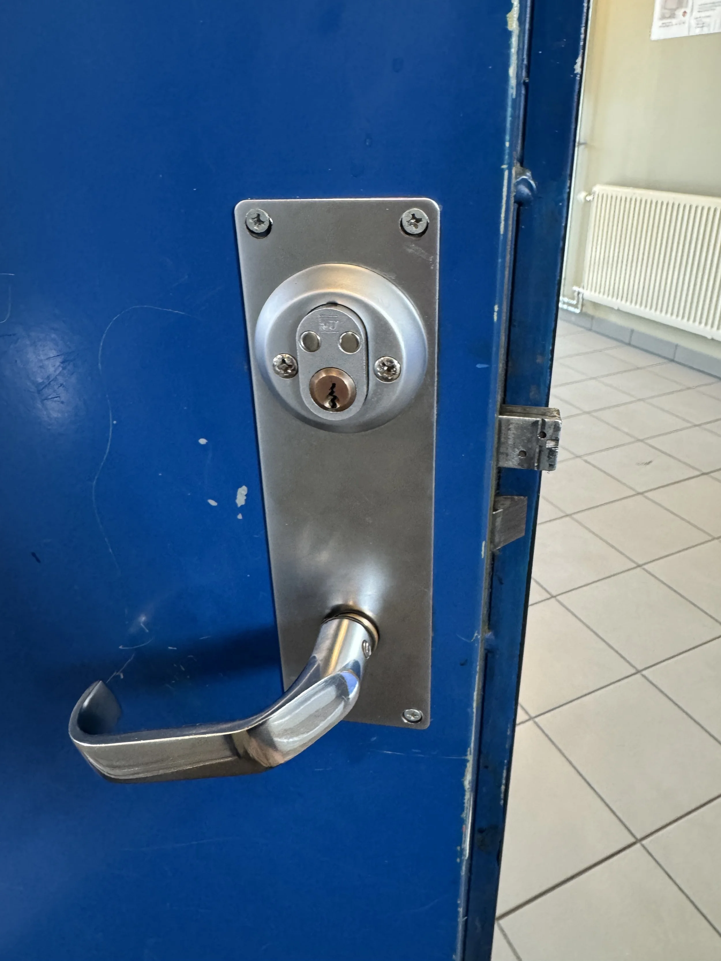 Nærbilde av en blå dør med en utvendig metall lås og dørhåndtak.