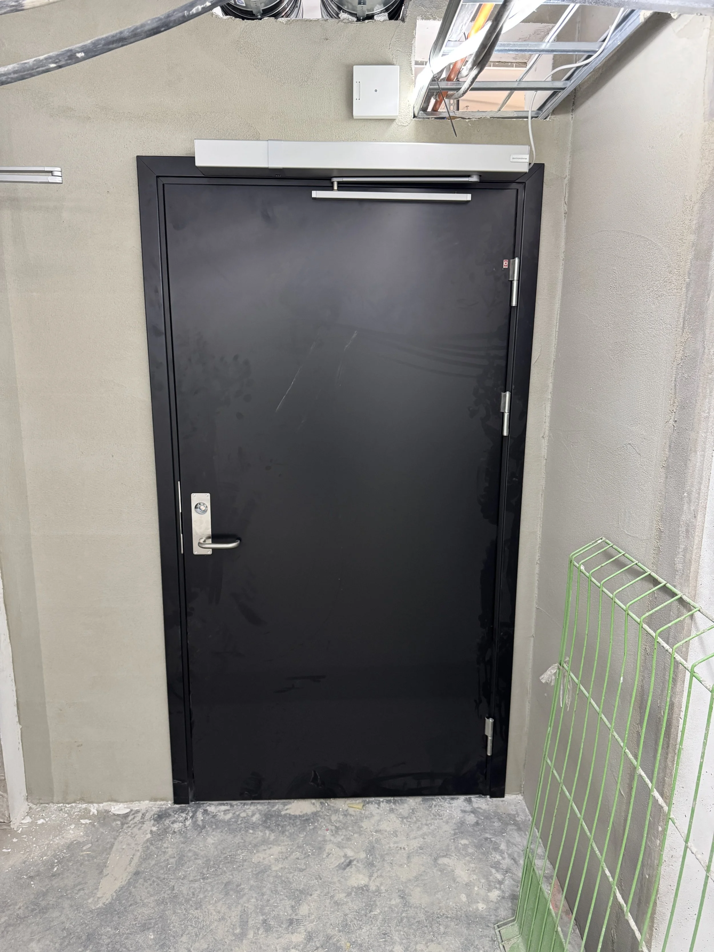 Sort dør i et byggeområde med metallhåndtak, omgitt av betongvegger og bygningsmaterialer