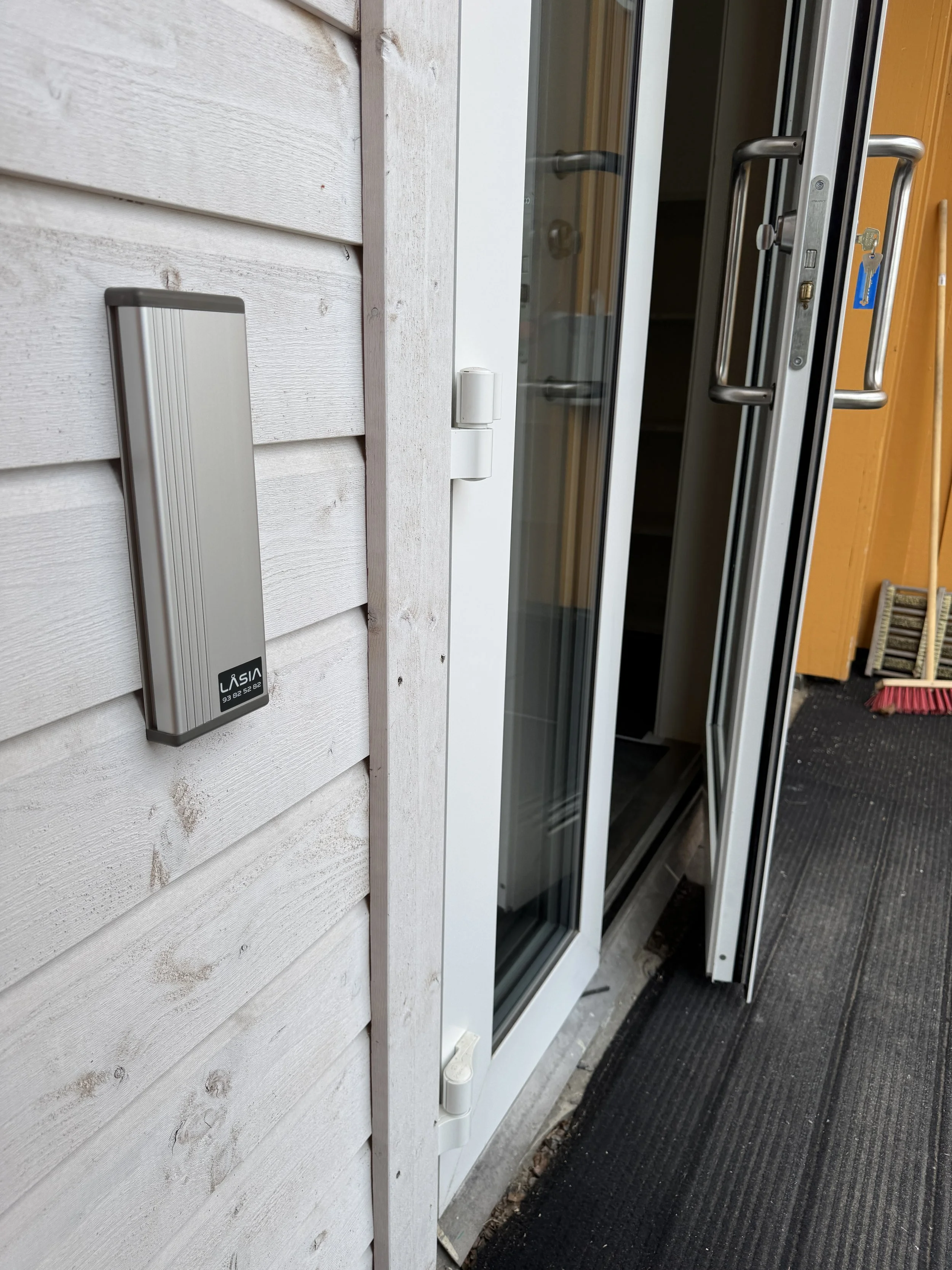 Nærbilde av en ytterdør med en digital lås på veggen ved siden av, på en terrasse med svart matte.