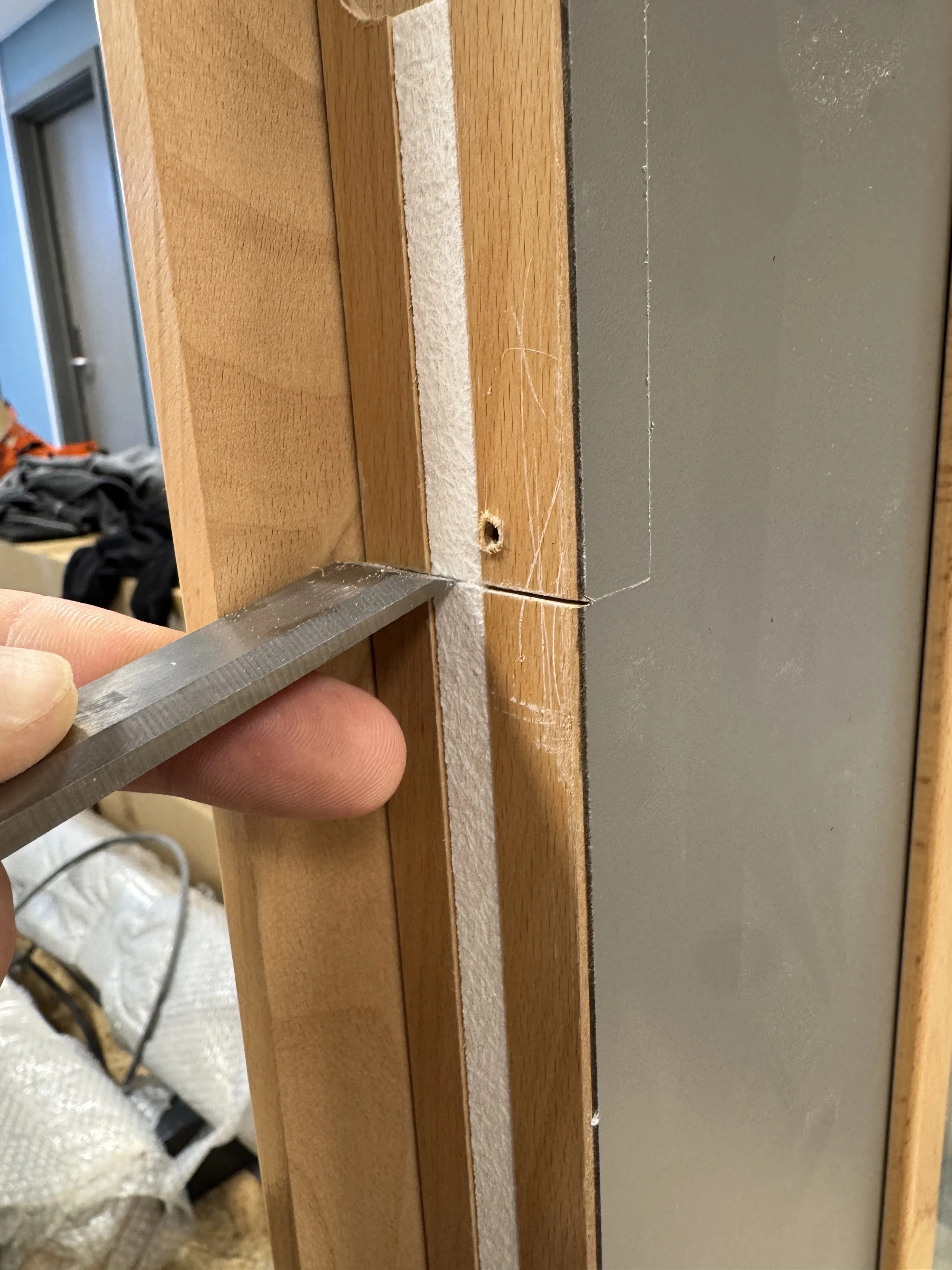 Nærbilde av en hånd som holder en skrujigg opp mot en forhåndsborret hull i en trefinish, i en byggefase.