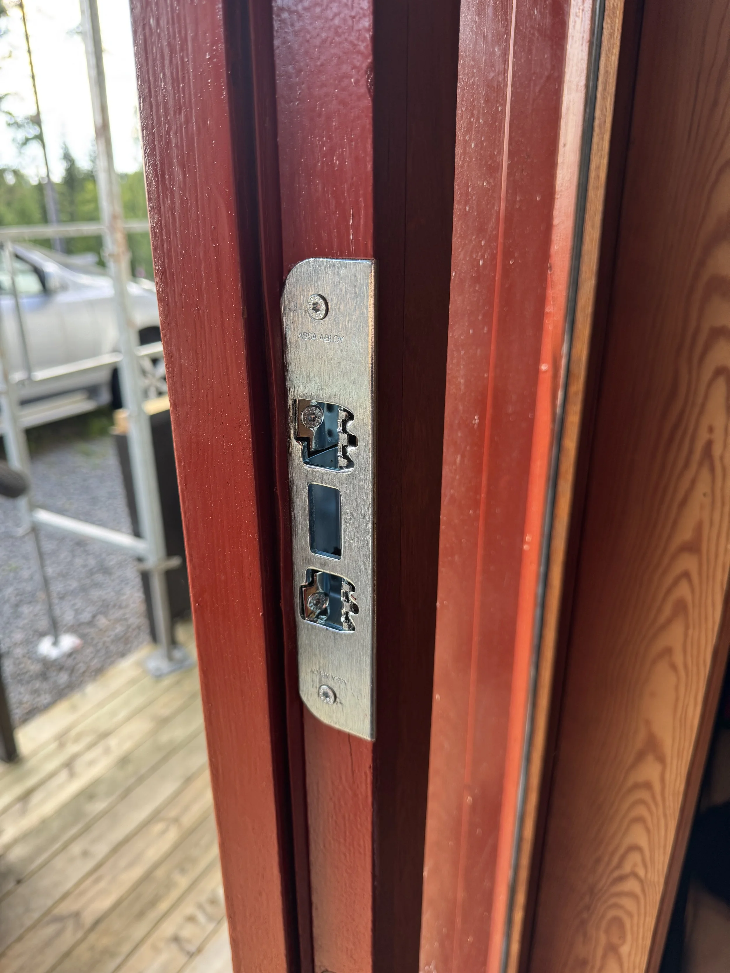 Nærbilde av et ufullstendig dørhengsel uten lås, montert på en rødfarget tretremdør.