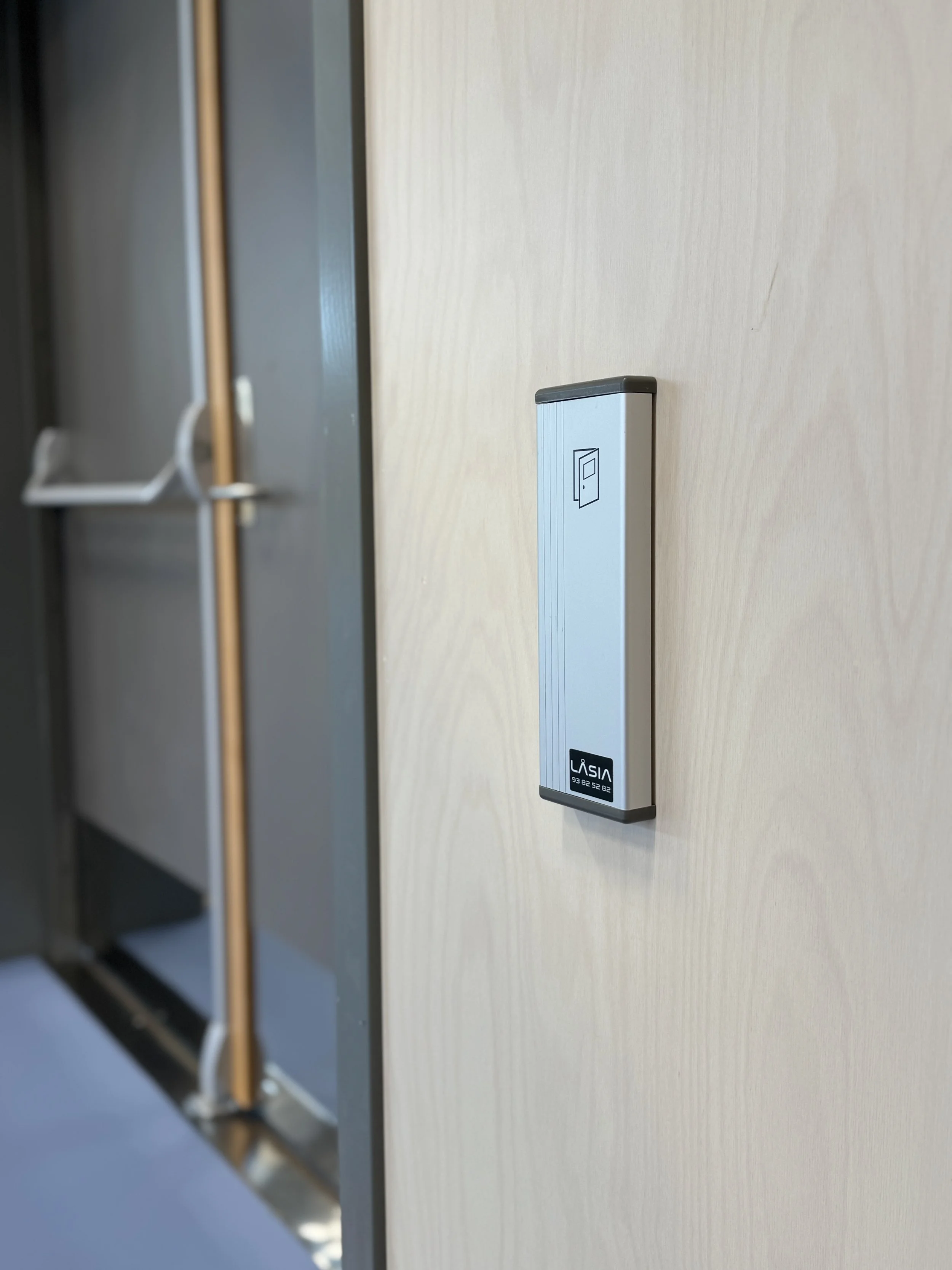 Nærbilde av en elektrisk dørtelefon med børstet aluminiumsbelegg som er montert på en lys trevegg.