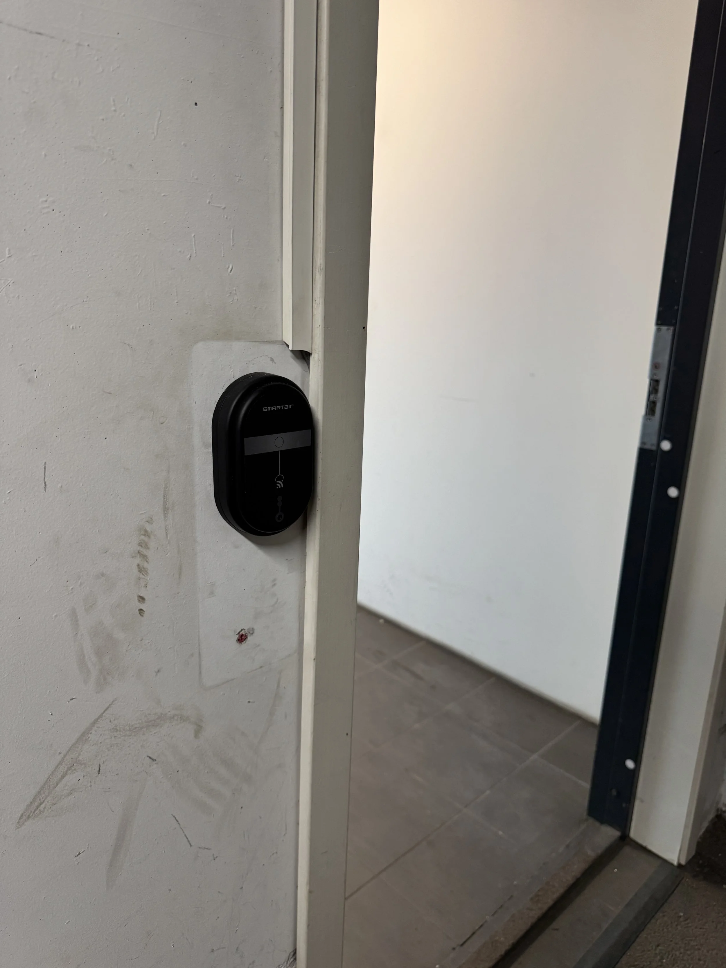 En dør med en svart elektronisk lås på innsiden og et skurt gulv.