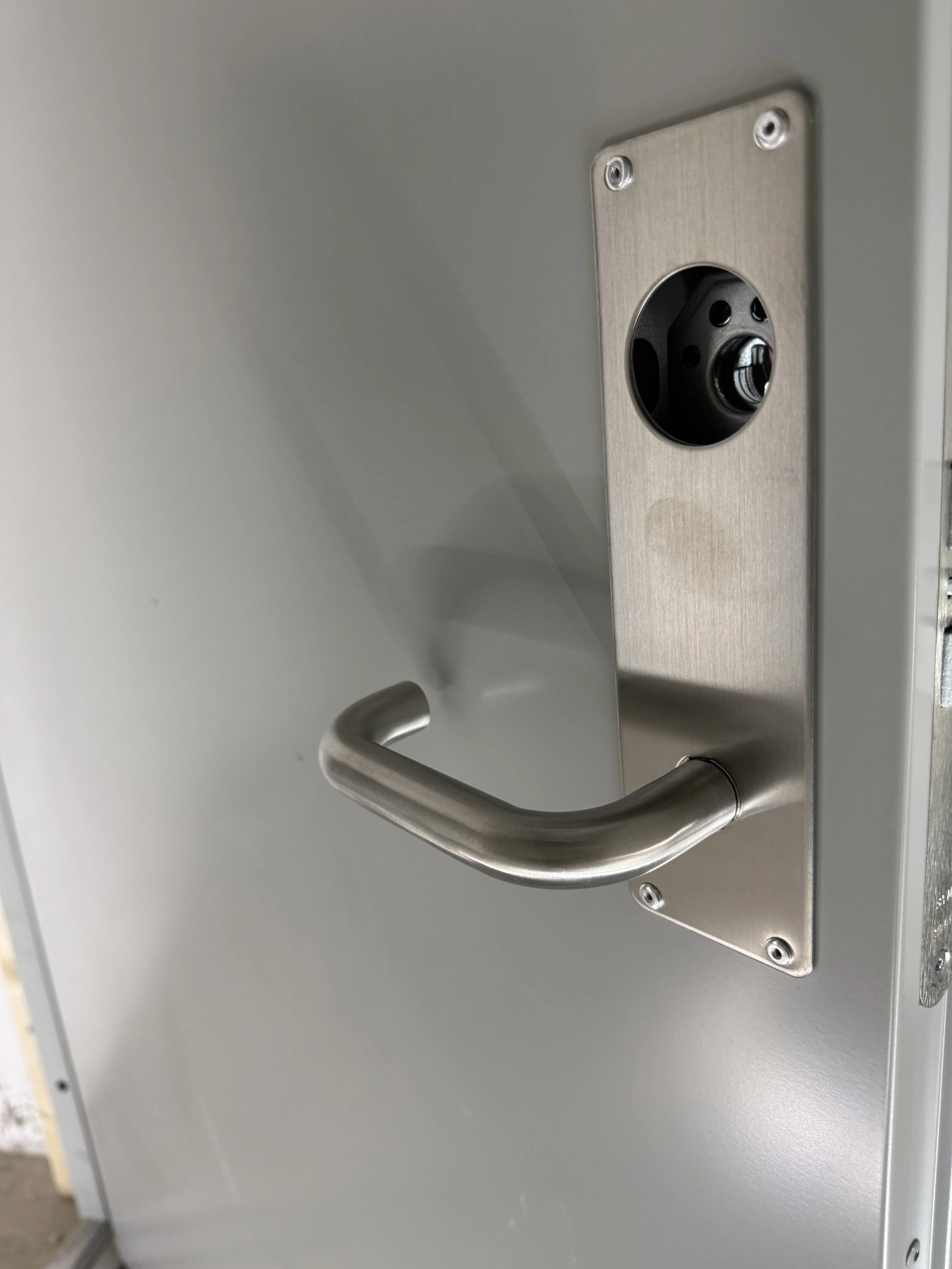 Nærbilde av en dørbeslag med håndtak og en lås med mekanisme. Døren er laget av metall og har skruer.