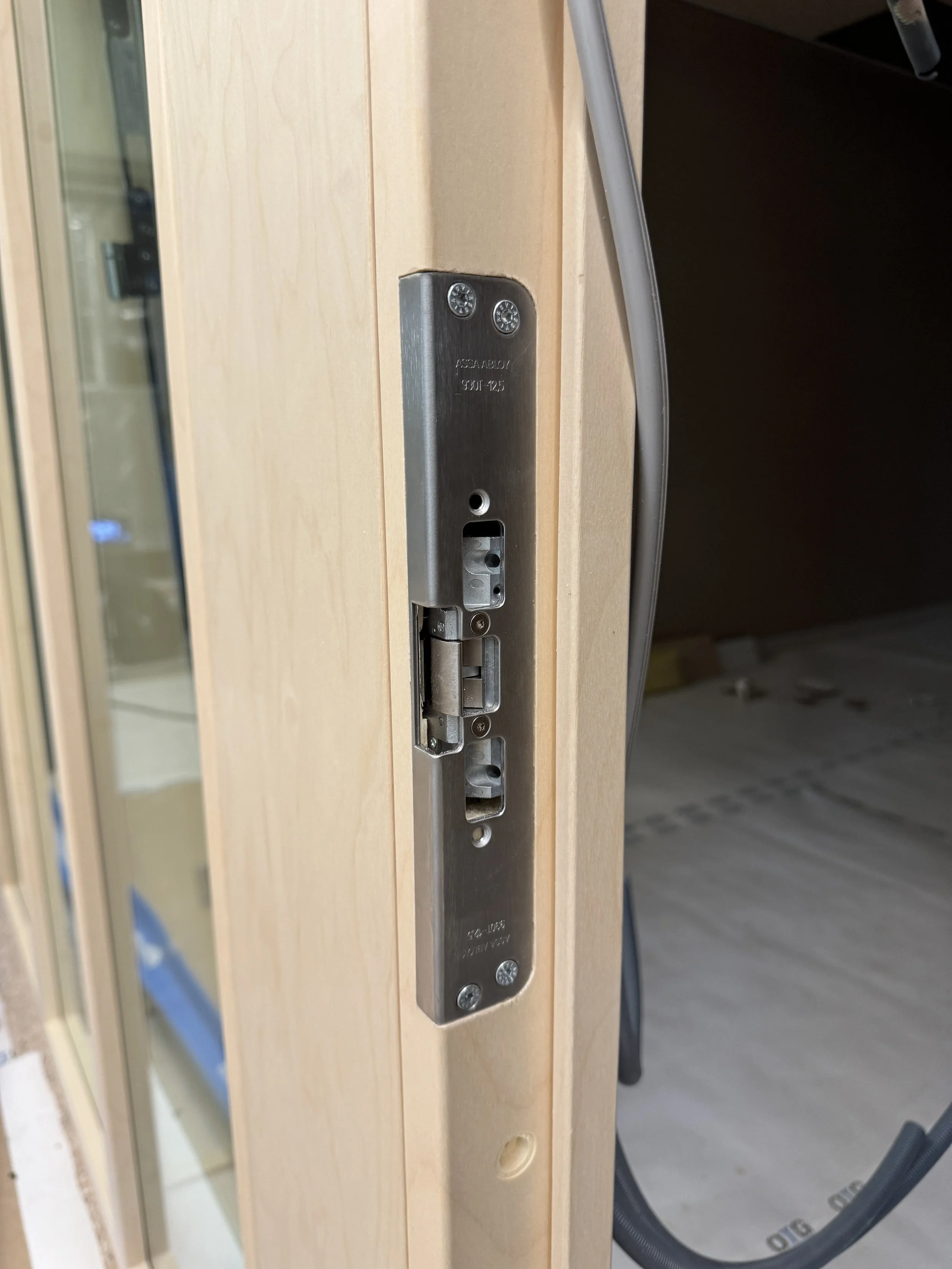 Nærbilde av en dørlåsinnfesting uten lås, montert på en trebjelke under bygging.