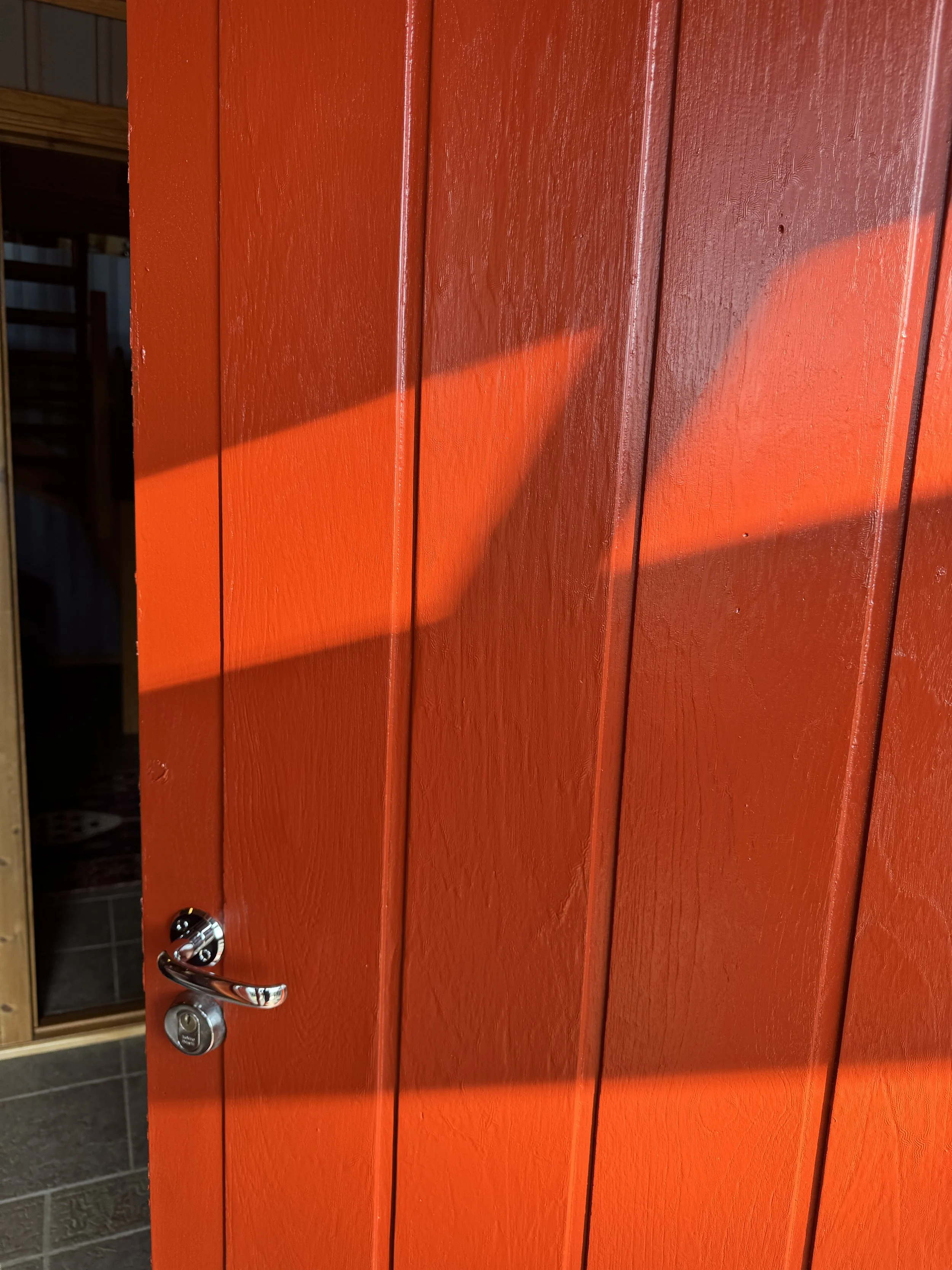 Rød malt polyesterdør med metallhåndtak og lås, utendørs.