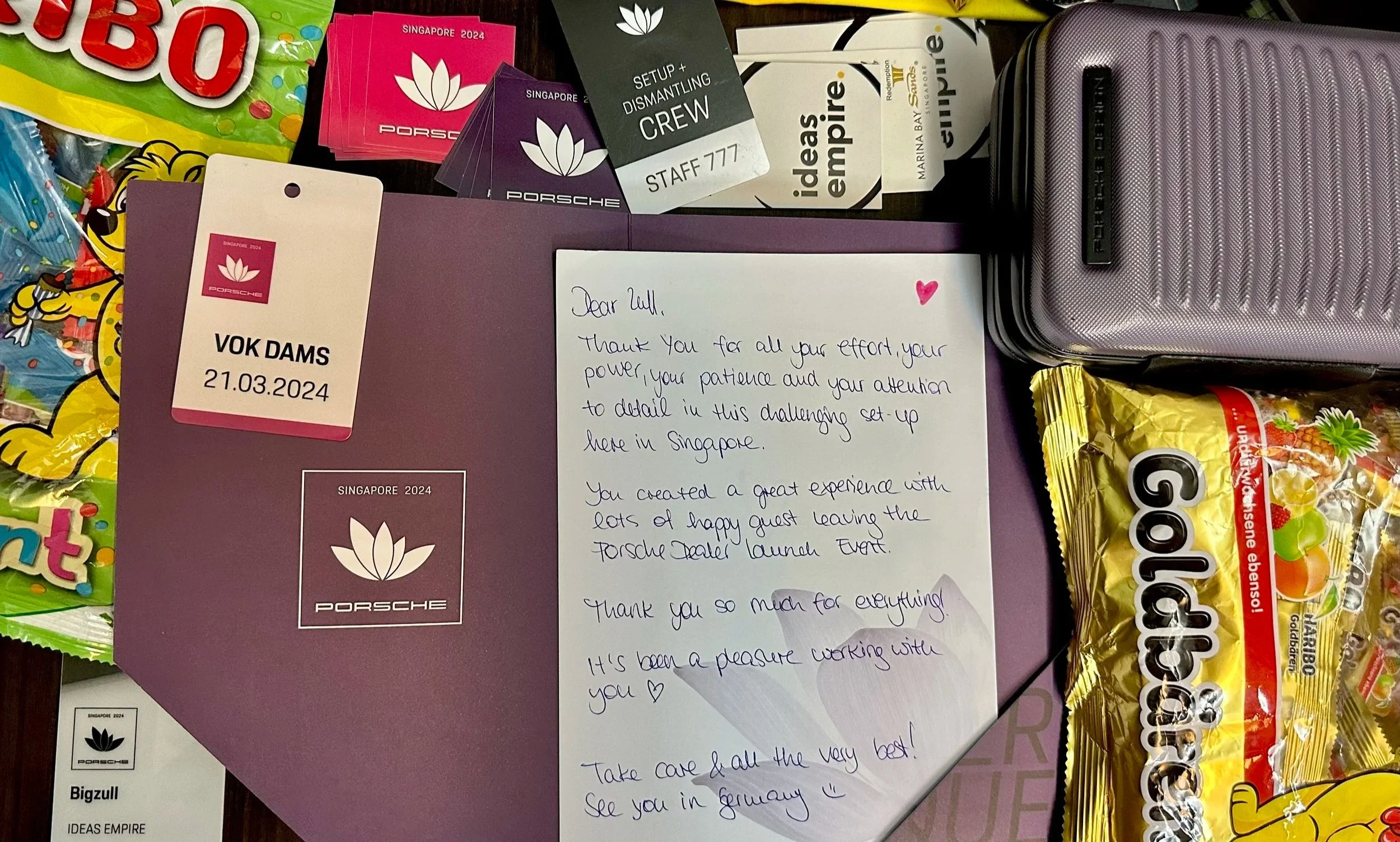 A collection of items including a handwritten letter, Porsche merchandise, candy, and travel accessories.