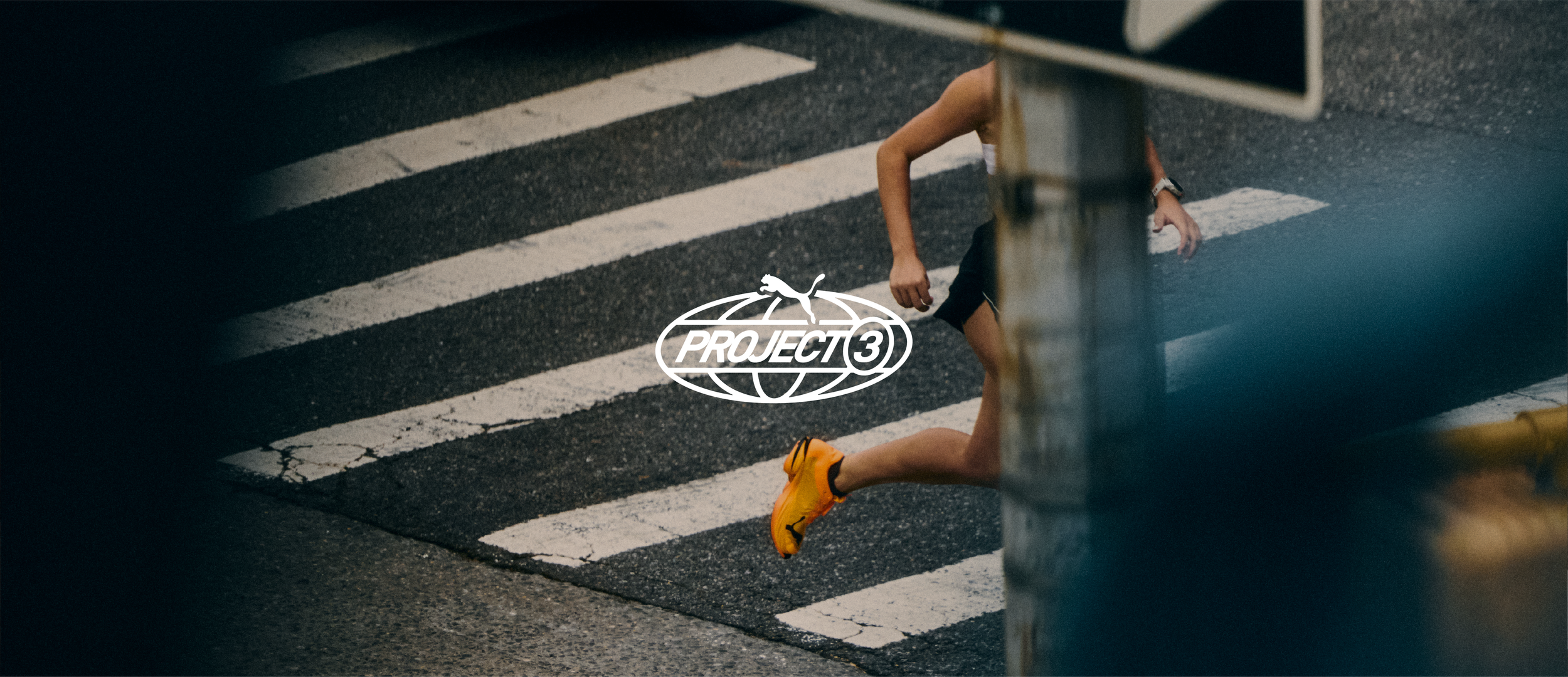 A person running across a crosswalk wearing bright yellow running shoes, a black shirt, and black shorts, with a logo for 'Project 3' and a puma symbol overlayed on the image.