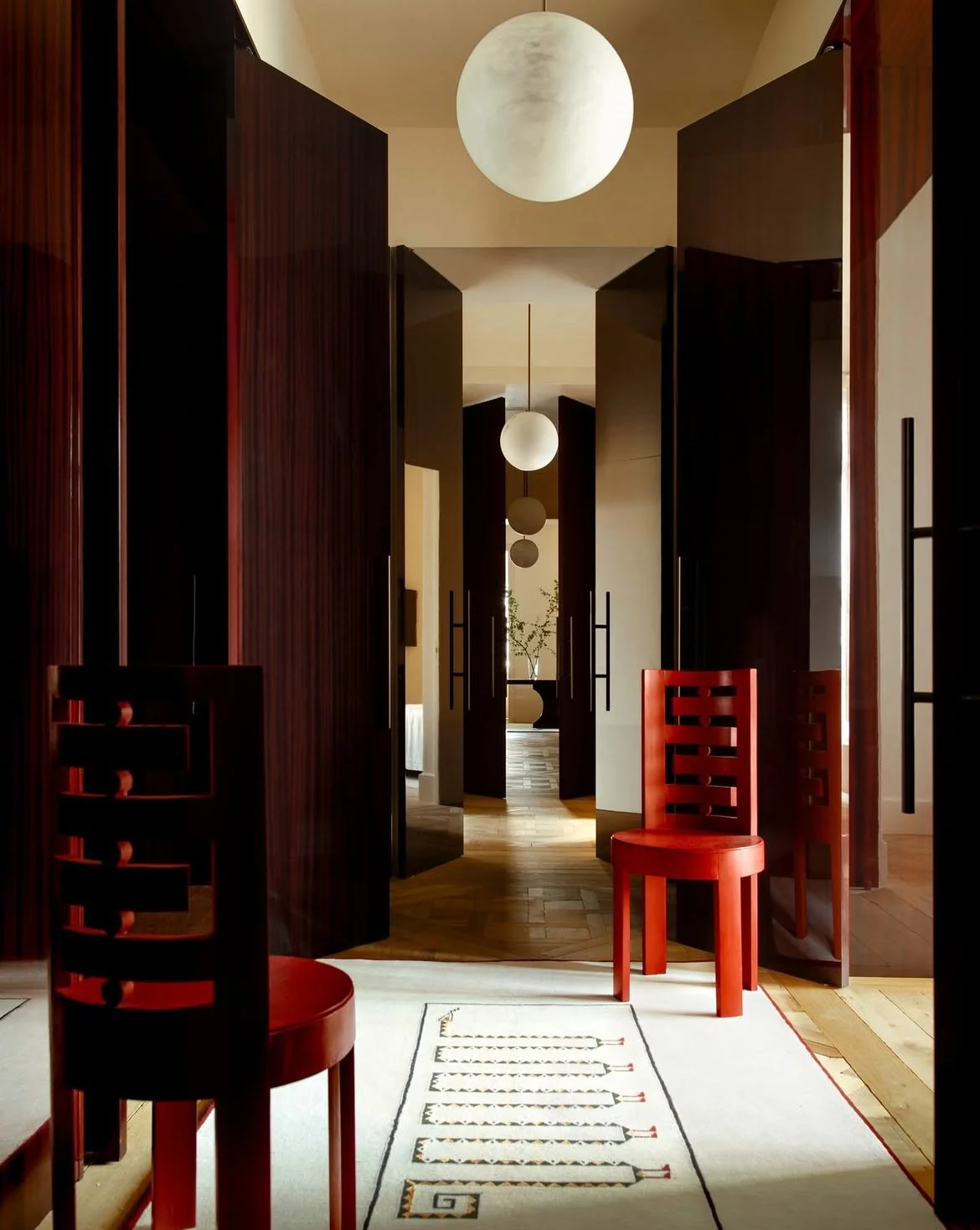 Pièce avec bois laqué rouge aux murs et assises rouge laquées, lampe globe au plafond et tapis au sol