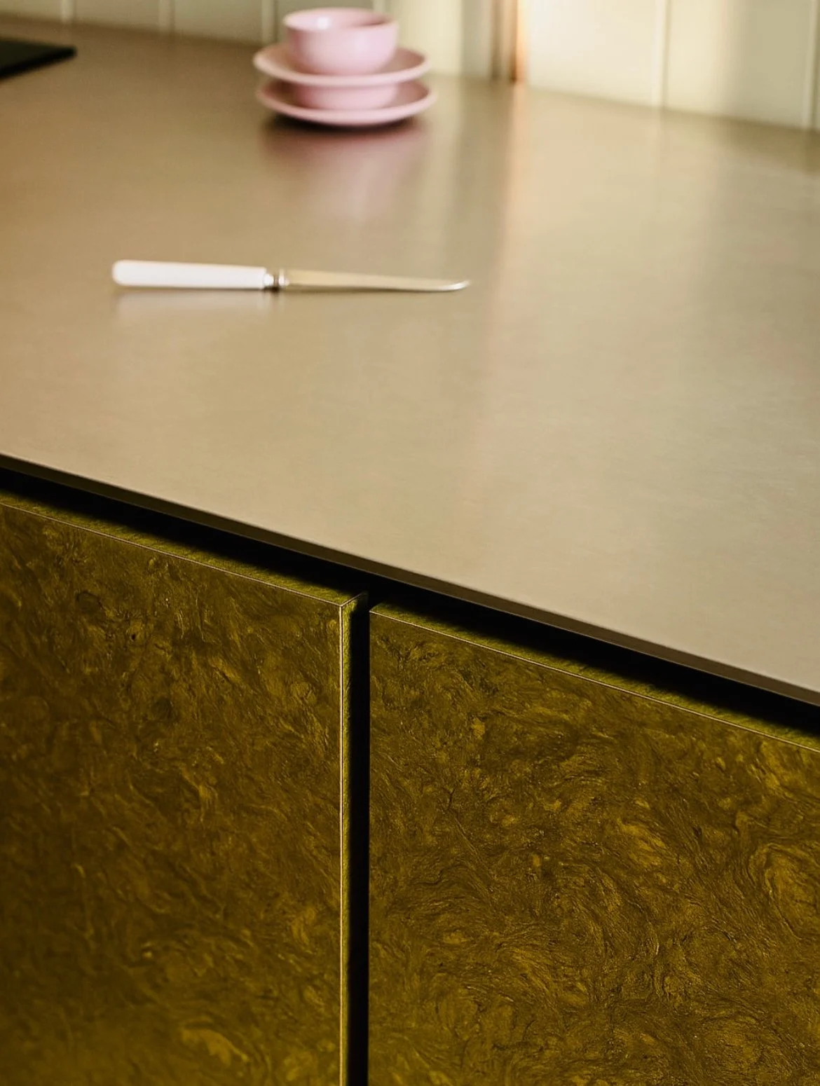 plan de travail cuisine avec meuble cuisine en liège teinté vert deux tasses roses en arrière plan et un couteau sur le plan de travail