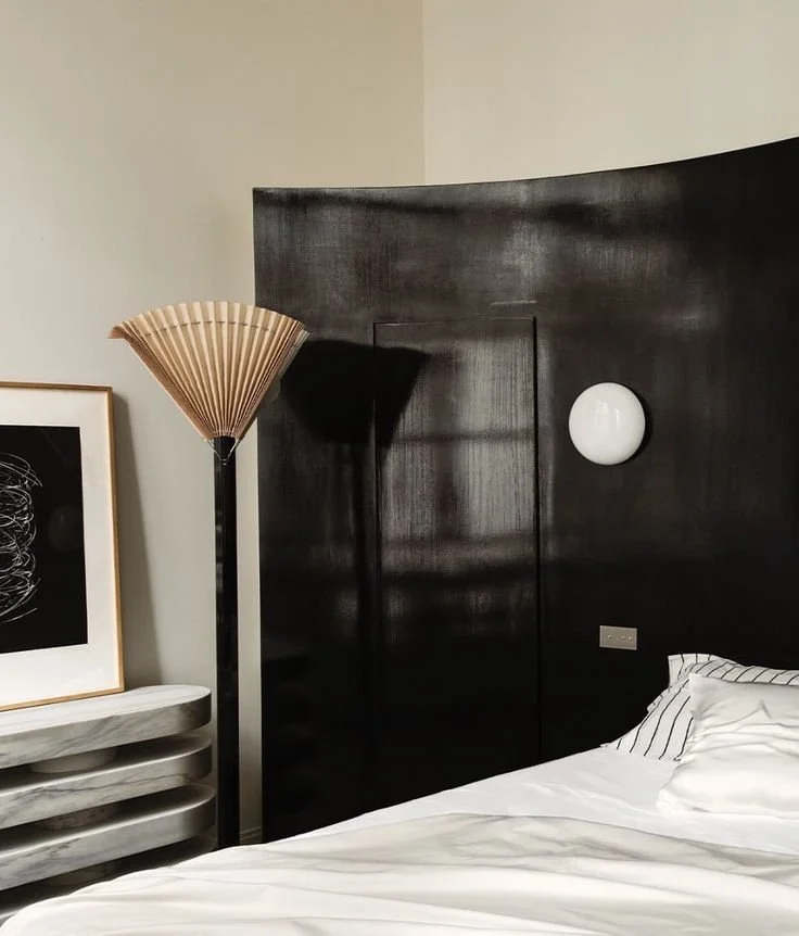 Une pièce crème aux murs, boiseries noires en tête de lit, applique opaline et lampe évantail