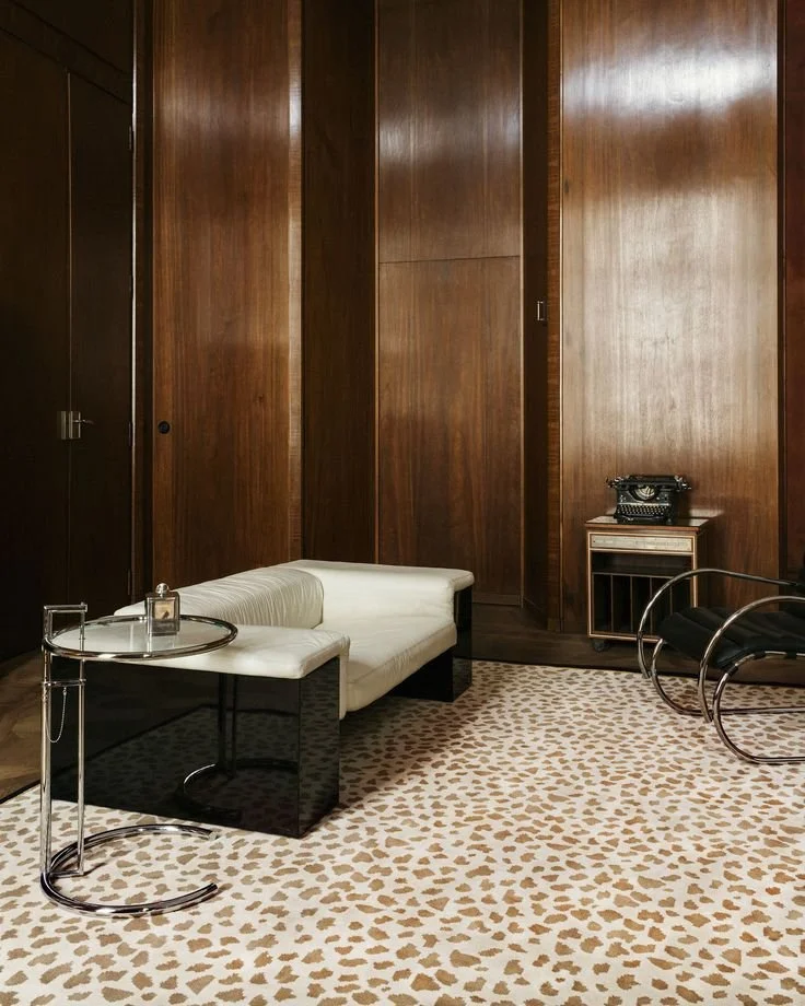 pièce boisée avec tapis nordic knots au sol, table d'appoint Eileen Grey, canapé laqué noir avec assise cuir beige