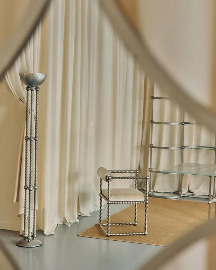 Intérieur avec rideaux beige aux murs et béton ciré au sol, collection mobilier en inox