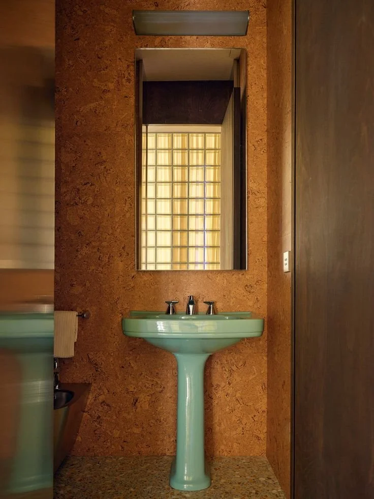 toilettes par RedDuo avec murs et sol en liège, vasque vintage couleur menthe, miroir au dessus de la vasque  