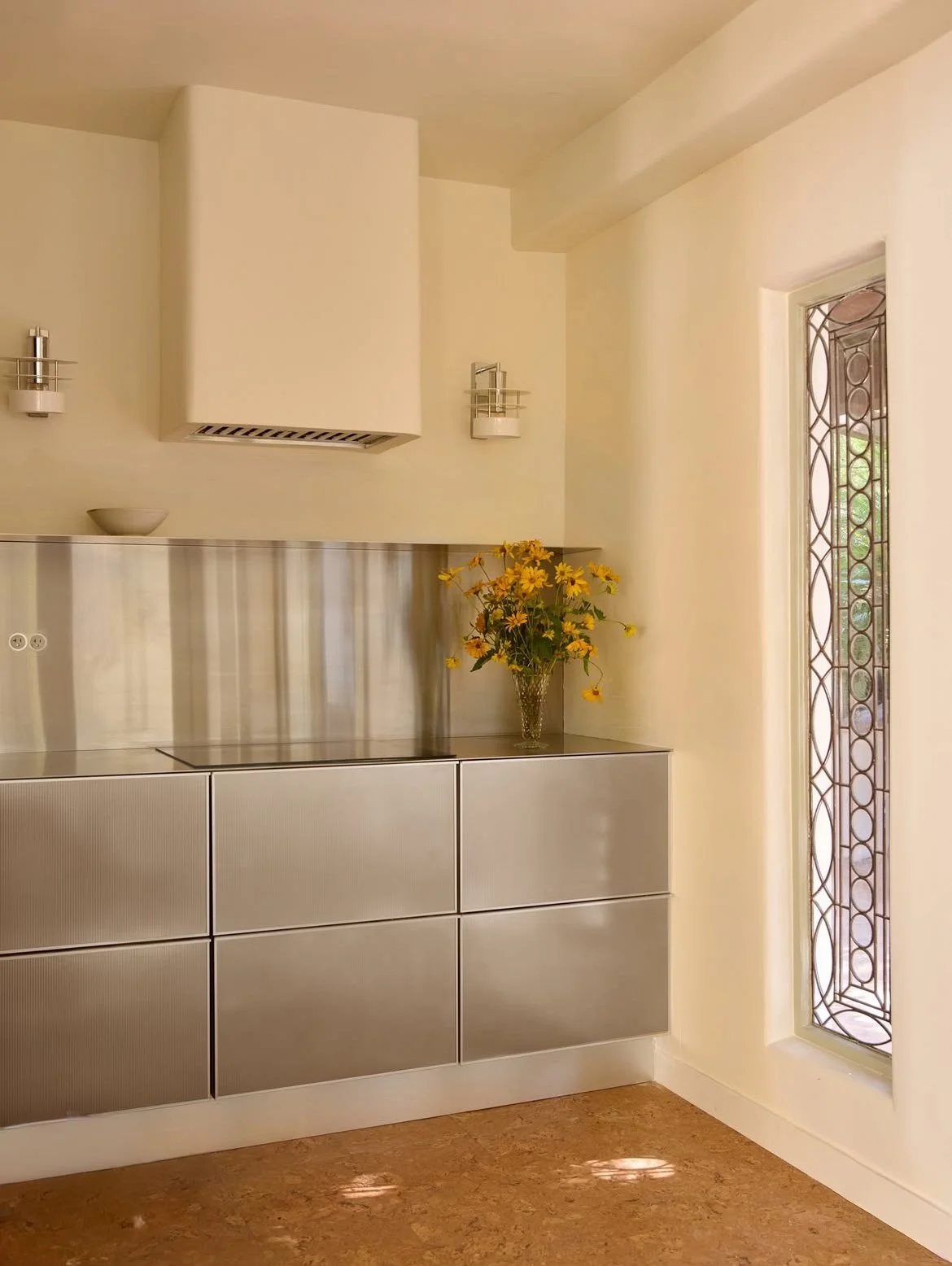 cuisine entièrement en inox avec sol en liège, peinture jaune beurre aux murs, niche avec ouverture sur l'extérieur