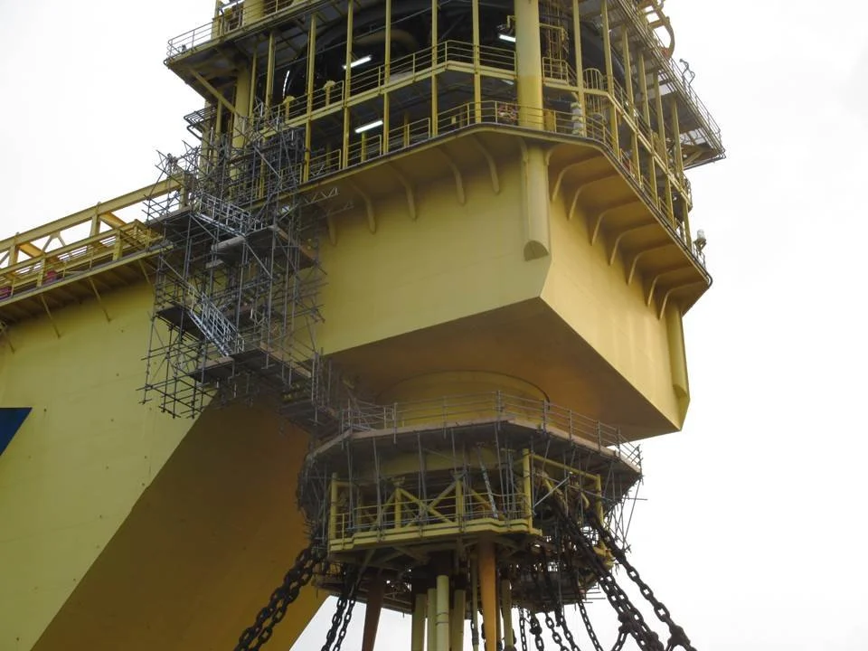 Close-up of a yellow offshore oil platform with scaffolding and safety railings.