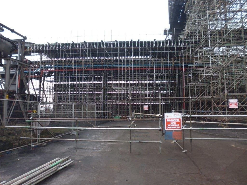Construction site with scaffolding and warning sign, indicating active work and safety concerns.