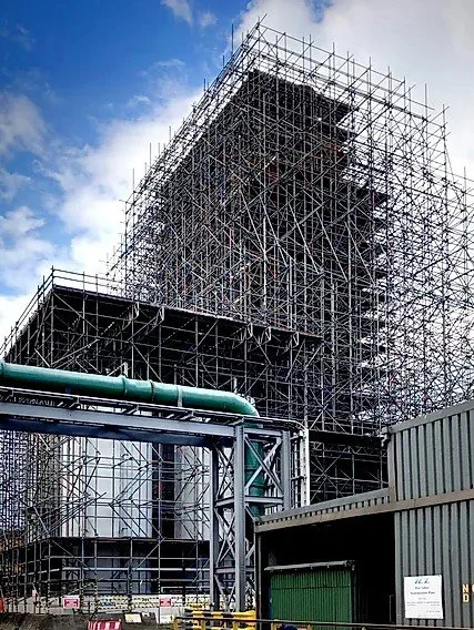 Construction site with metal scaffolding around a tall building under construction against a partly cloudy sky.