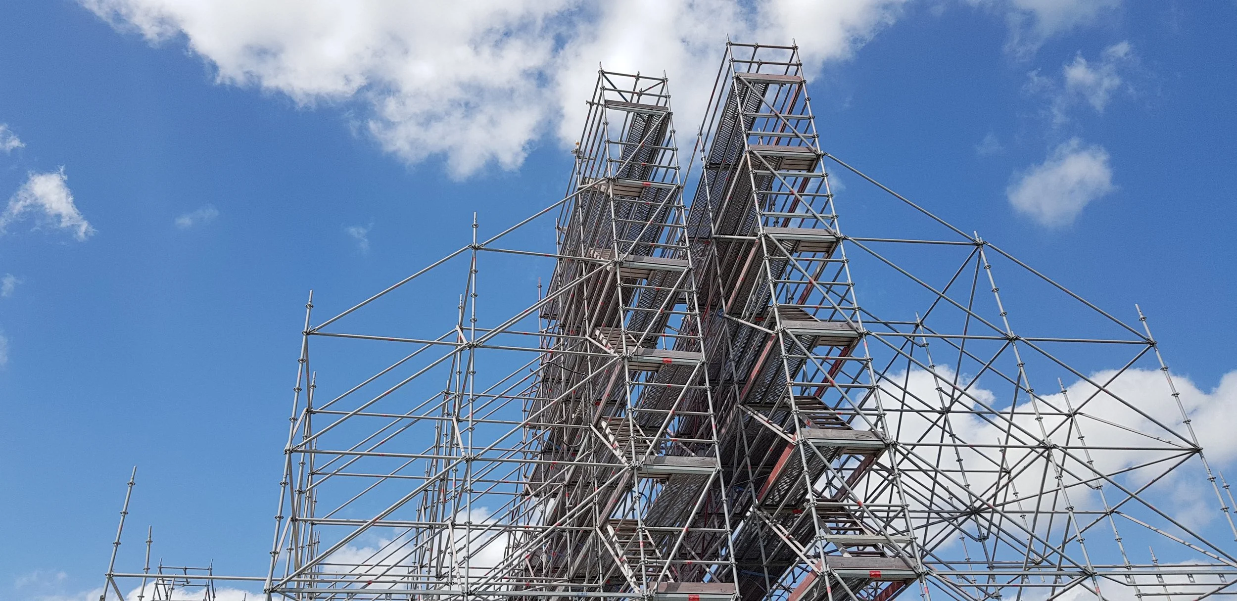 Metal scaffolding structure against a blue sky with scattered white clouds.