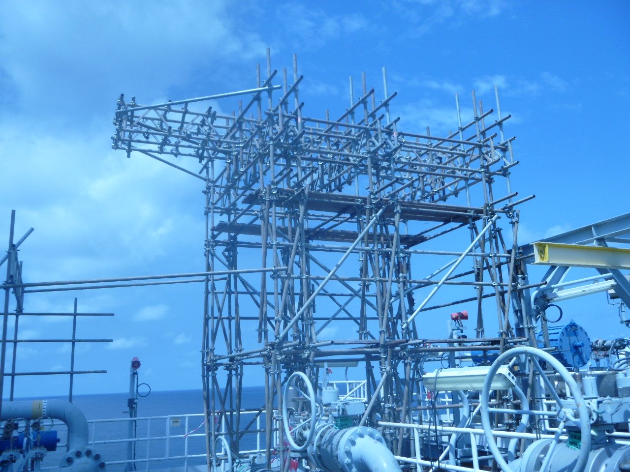 A complex metal scaffolding structure on a ship against a partly cloudy blue sky.