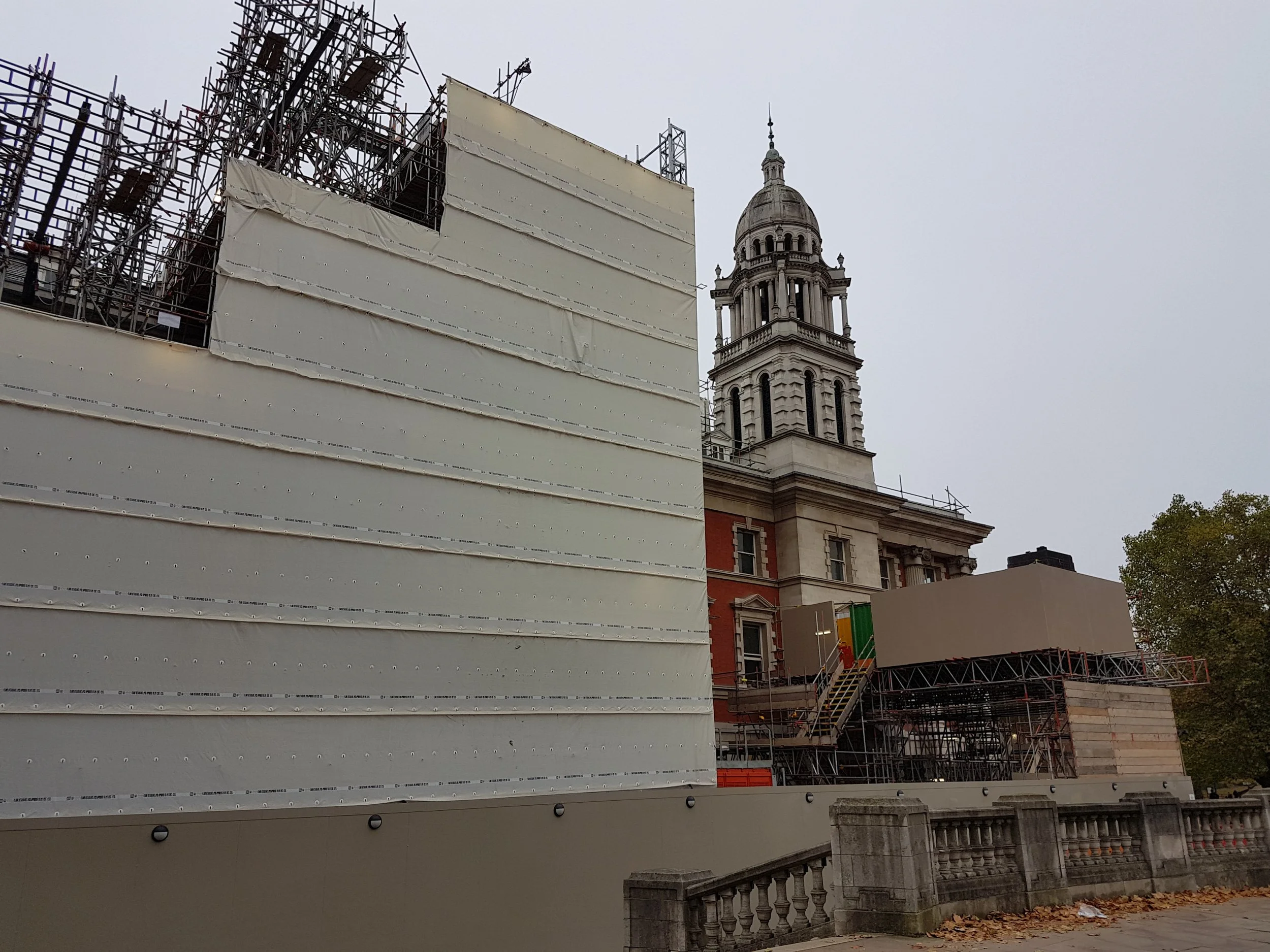 Construction scaffolding and temporary barriers surround a historic building with a prominent bell tower.