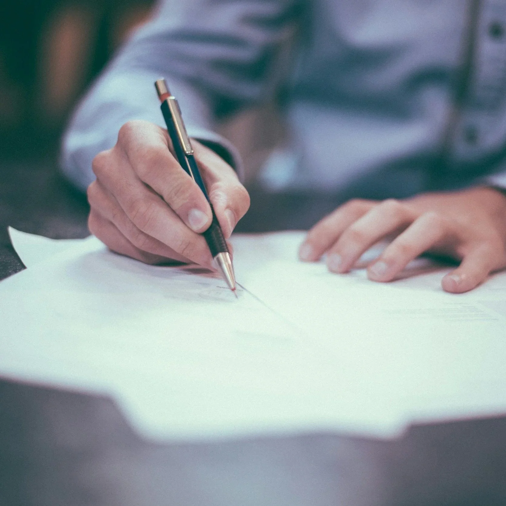 A person is writing or signing a document with a pen on paper.