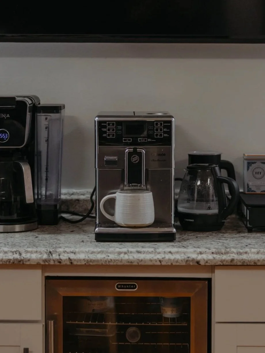Countertop with a coffee maker, a coffee mug, a kettle, and other appliances on an office counter.