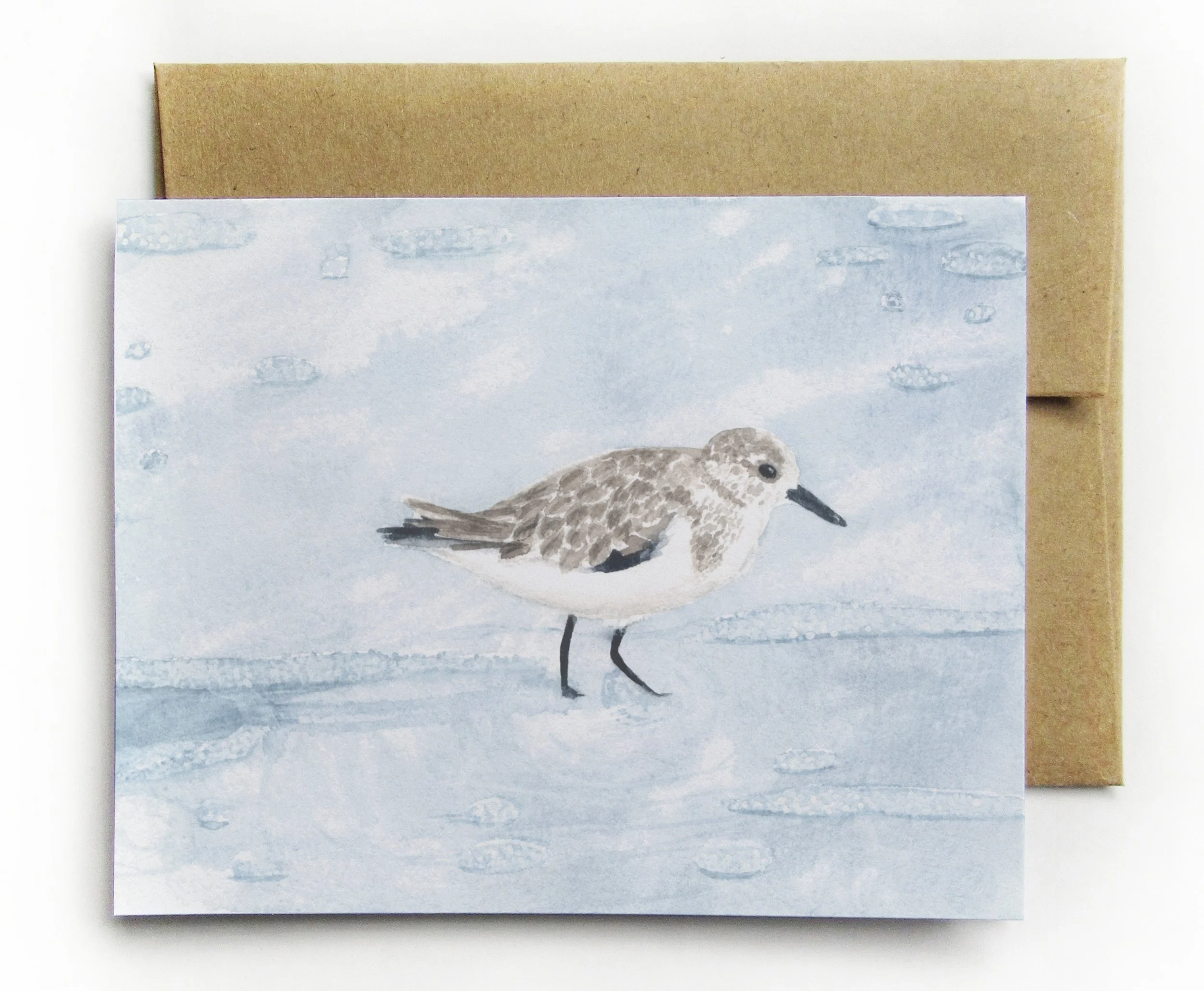 A closeup of Watercolor sandpiper standing with a soft light blue background on a blank greeting card on linen textured cardstock.