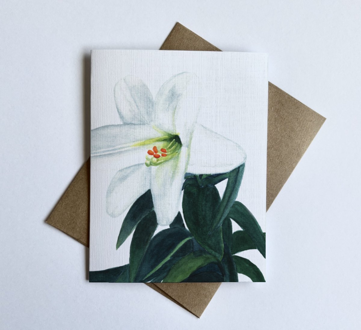 Watercolor Easter lily art on linen-textured cardstock, featuring soft white petals and green leaves.