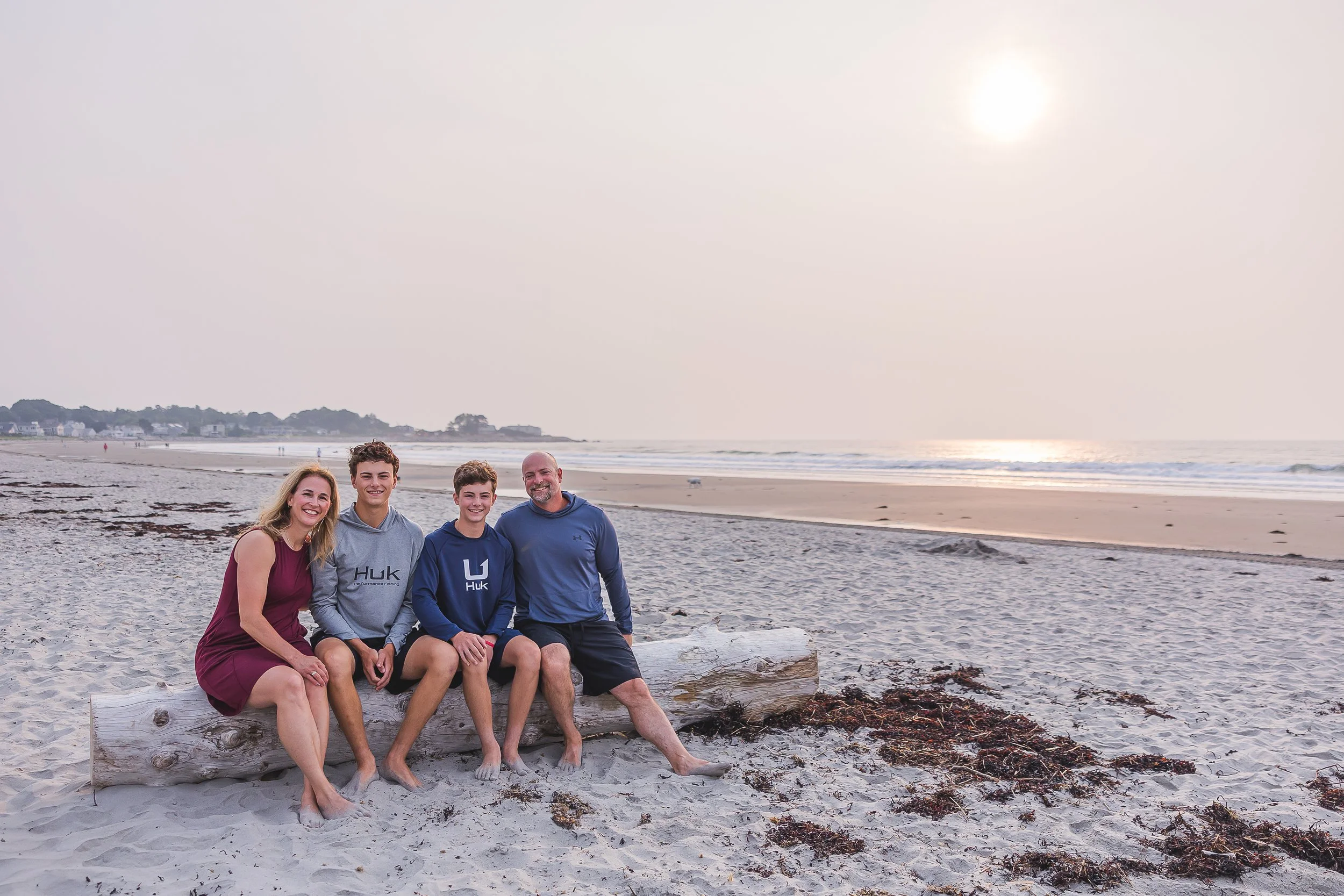 family of 4 seated on beach wood at sunrise at a NH beach