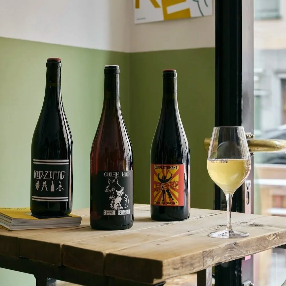 Tre vinflaskor på ett träbord. Ett vinglas fyllt med naturligt vin.