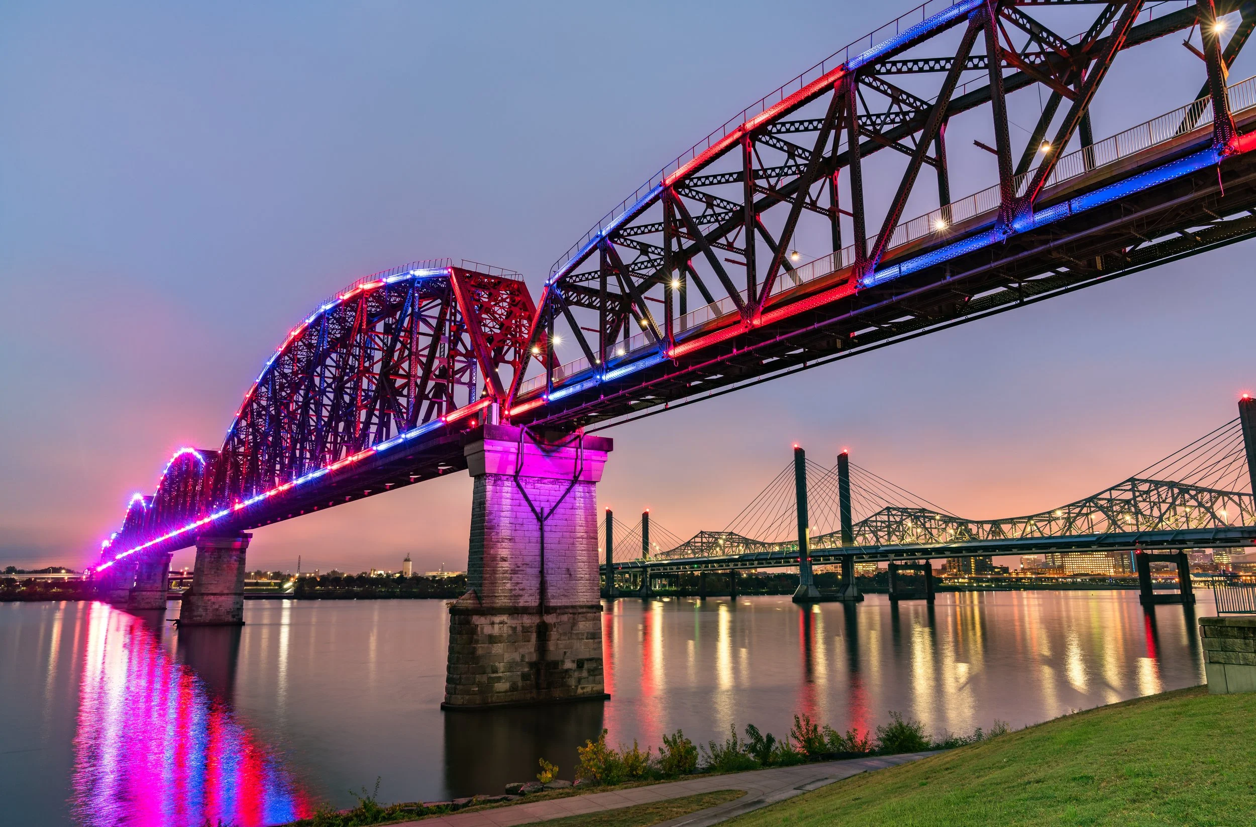 A bridge over a river decorated with colorful lights at sunset.