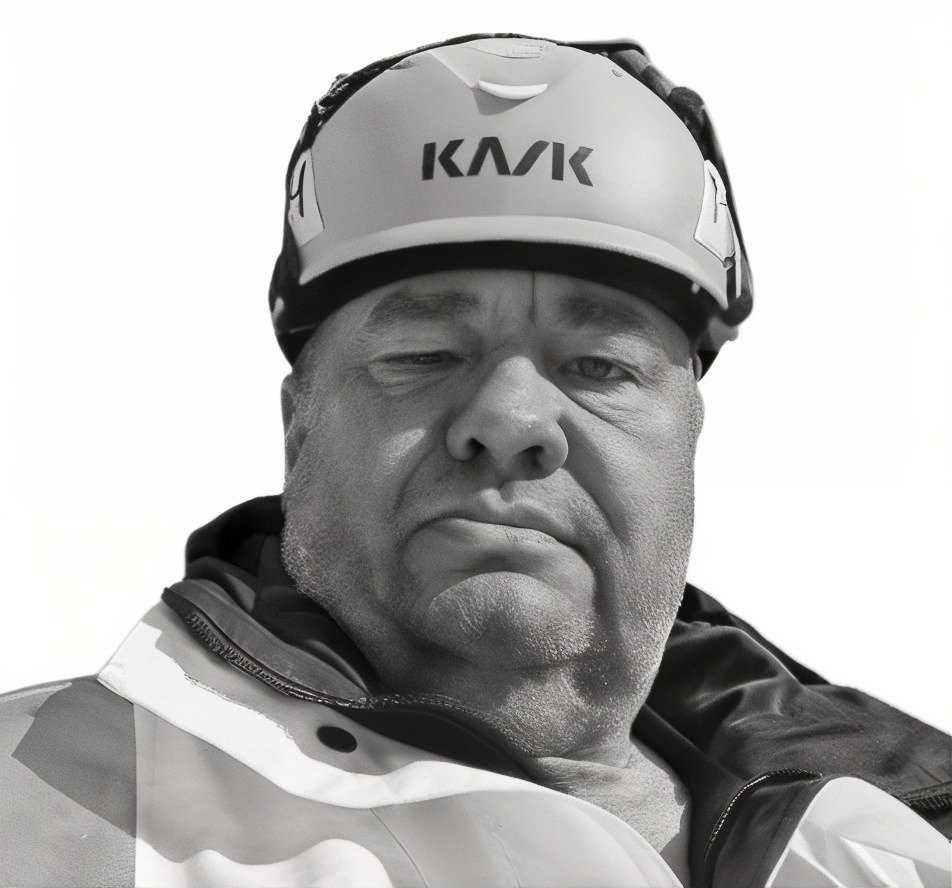 A man wearing a motorcycle helmet and riding gear, taking a selfie with a neutral expression.