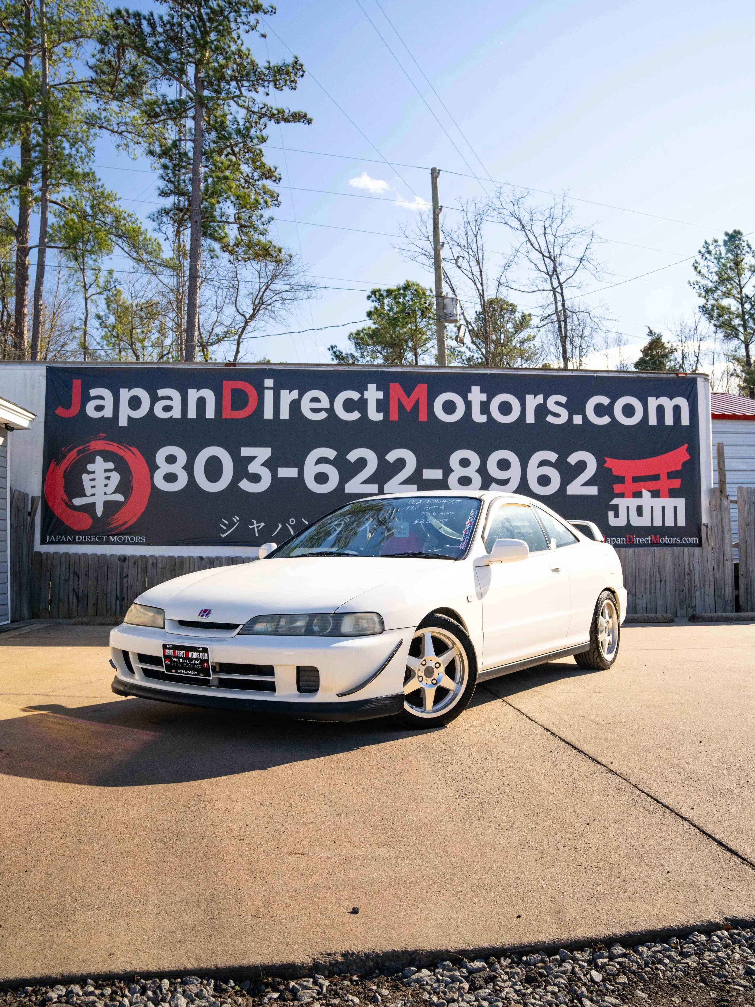 White RHD Imported Honda Integra parked in front of a large sign for Japan Direct Motors dealership