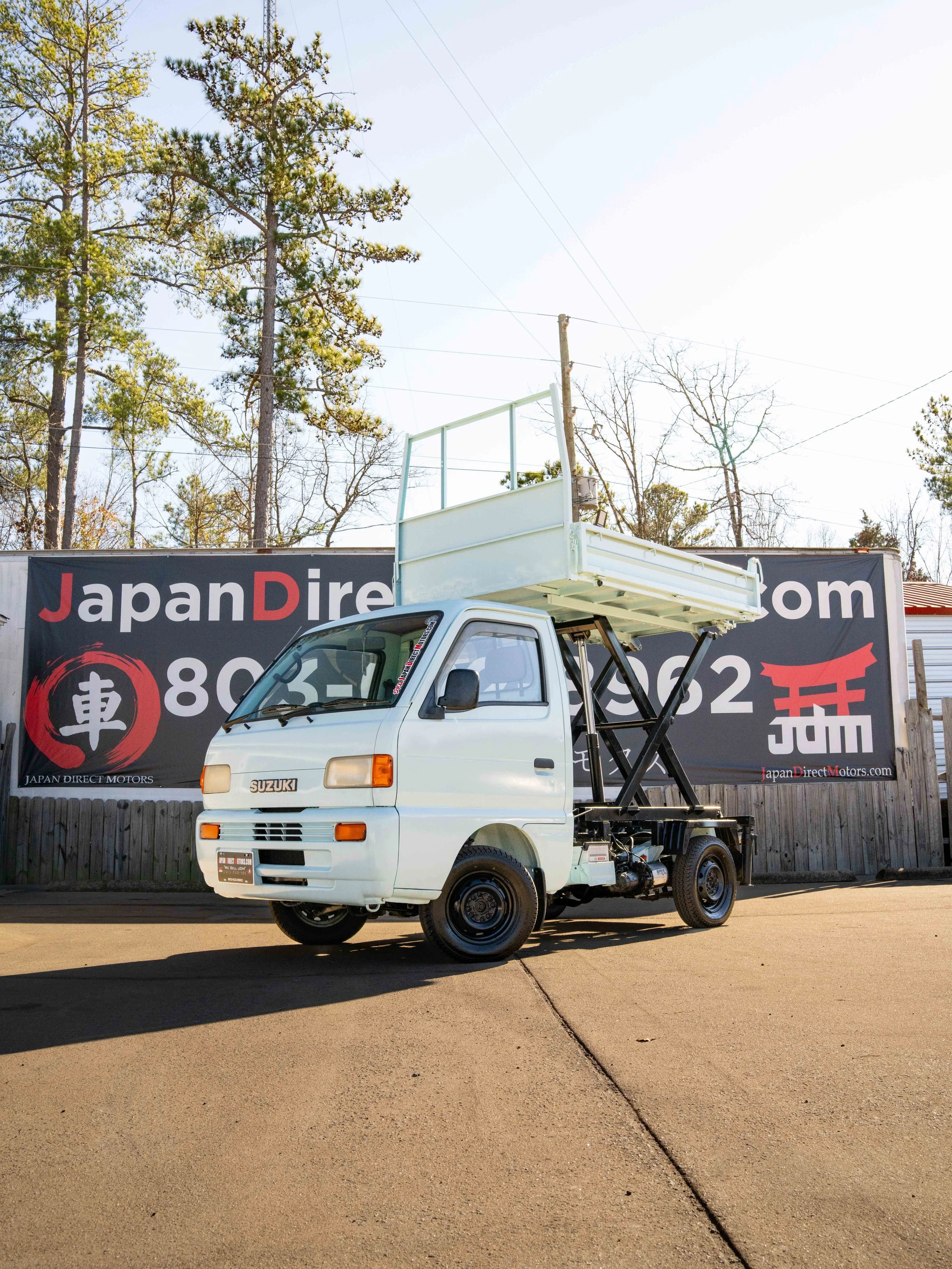 Suzuki Carry Siccor lift / dump truck parked in front of Japan Direct Motors sign