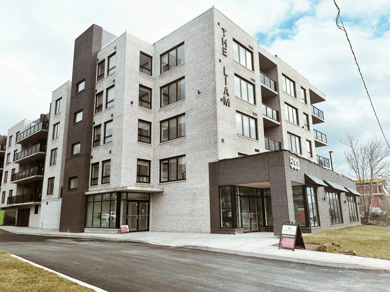 Modern multi-story apartment building with white and dark brick exterior, balconies, and a corner entrance, located at 533 on a cloudy day.