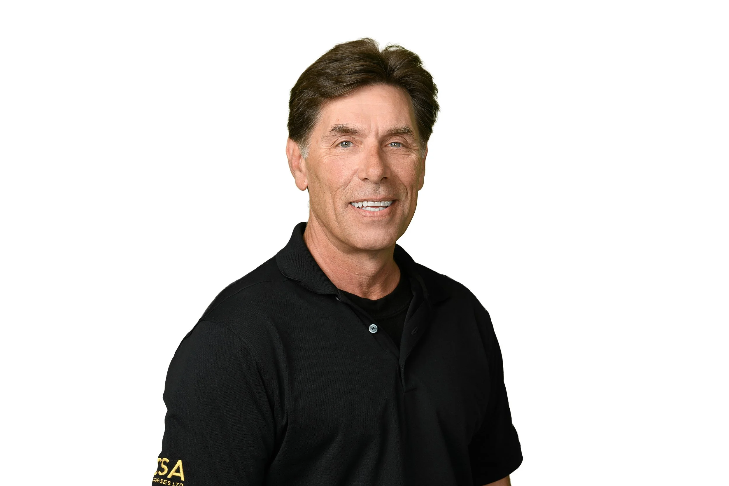 A middle-aged man with brown hair styled to the side, wearing a black polo shirt with a logo on the sleeve, smiling against a plain white background.
