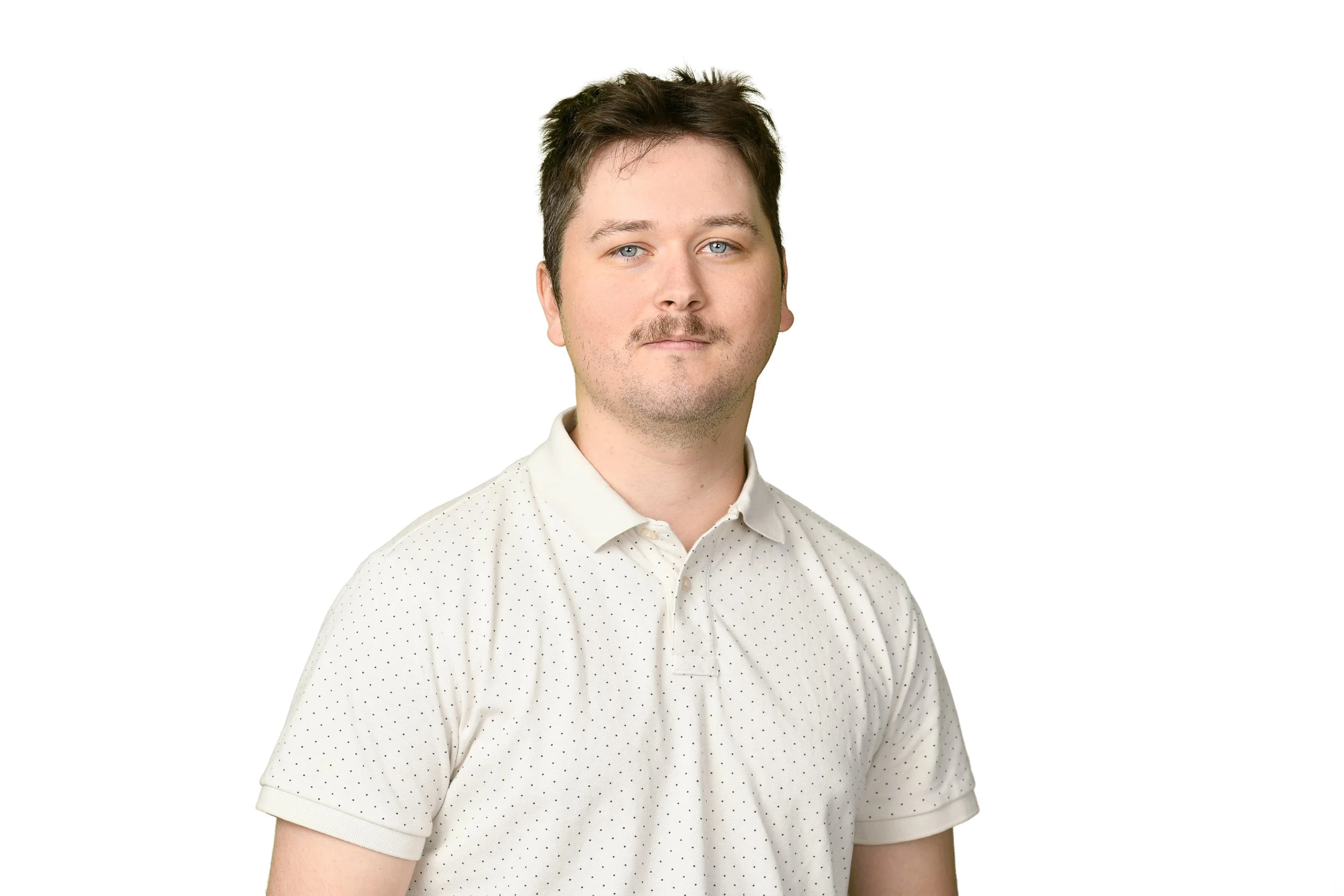 A young man with short brown hair, blue eyes, and light facial hair, wearing a white short-sleeved button-up shirt with small black dots, standing against a plain white background.