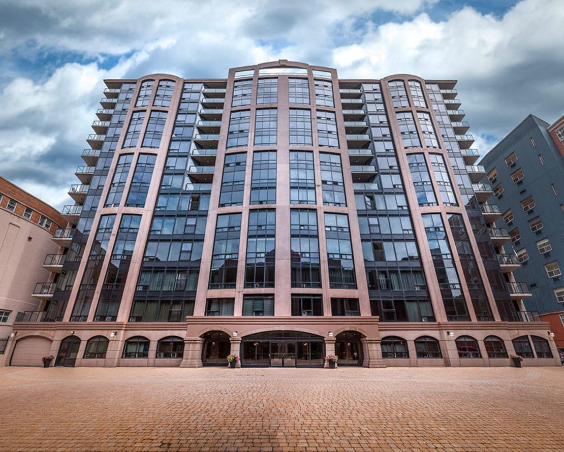 Modern multi-story apartment building with large glass windows and balconies, set against a cloudy sky.
