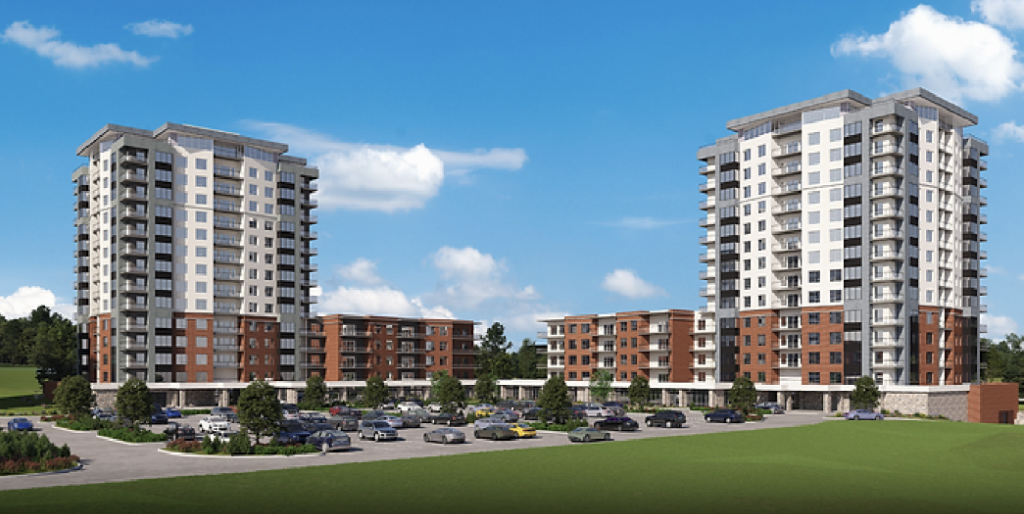 Two modern multi-story apartment buildings with parking lots and landscaped greenery in front, under a bright blue sky with scattered clouds.