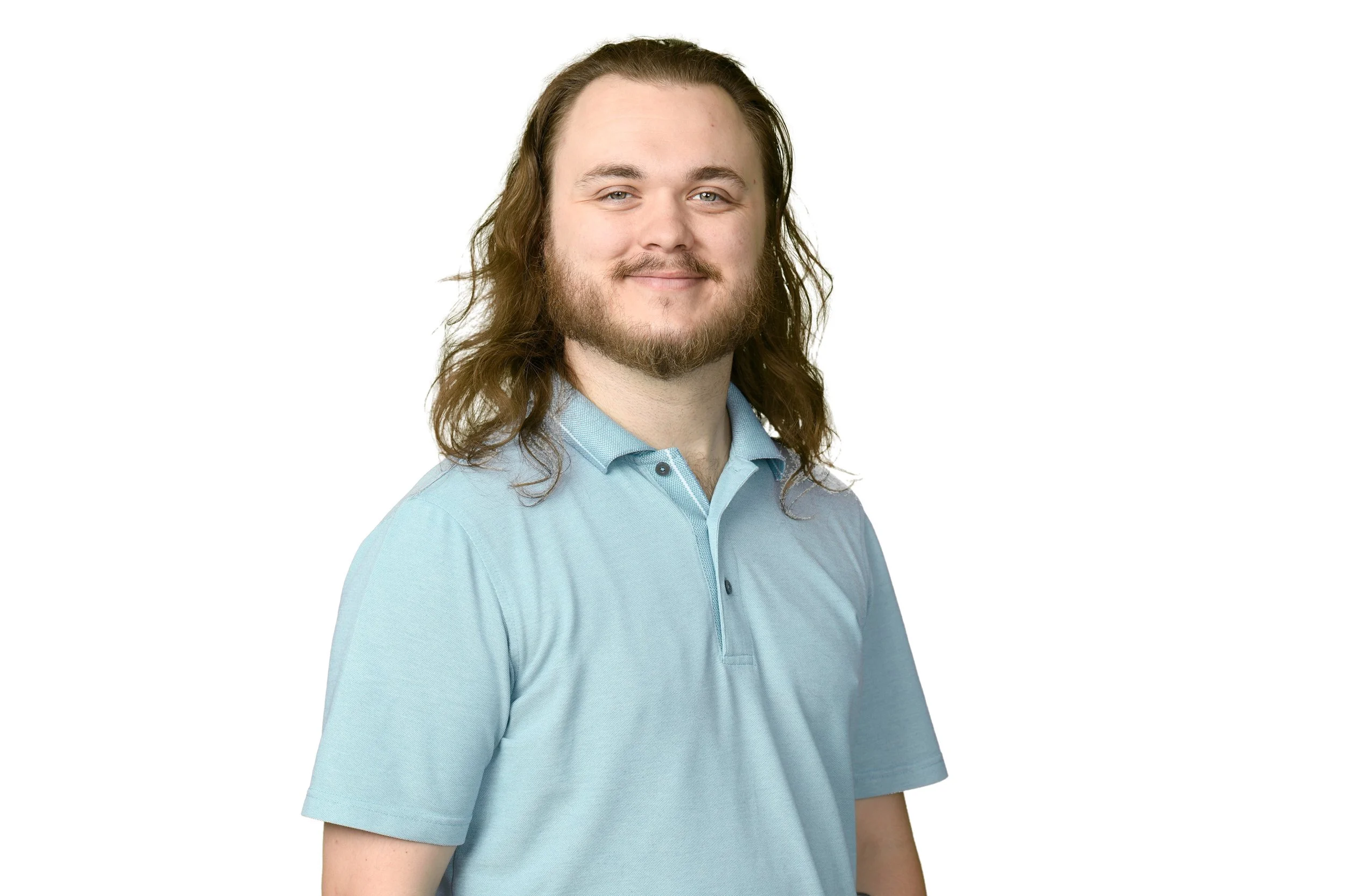 A man with long brown hair, a beard, and mustache, smiling, wearing a light blue polo shirt against a plain white background.