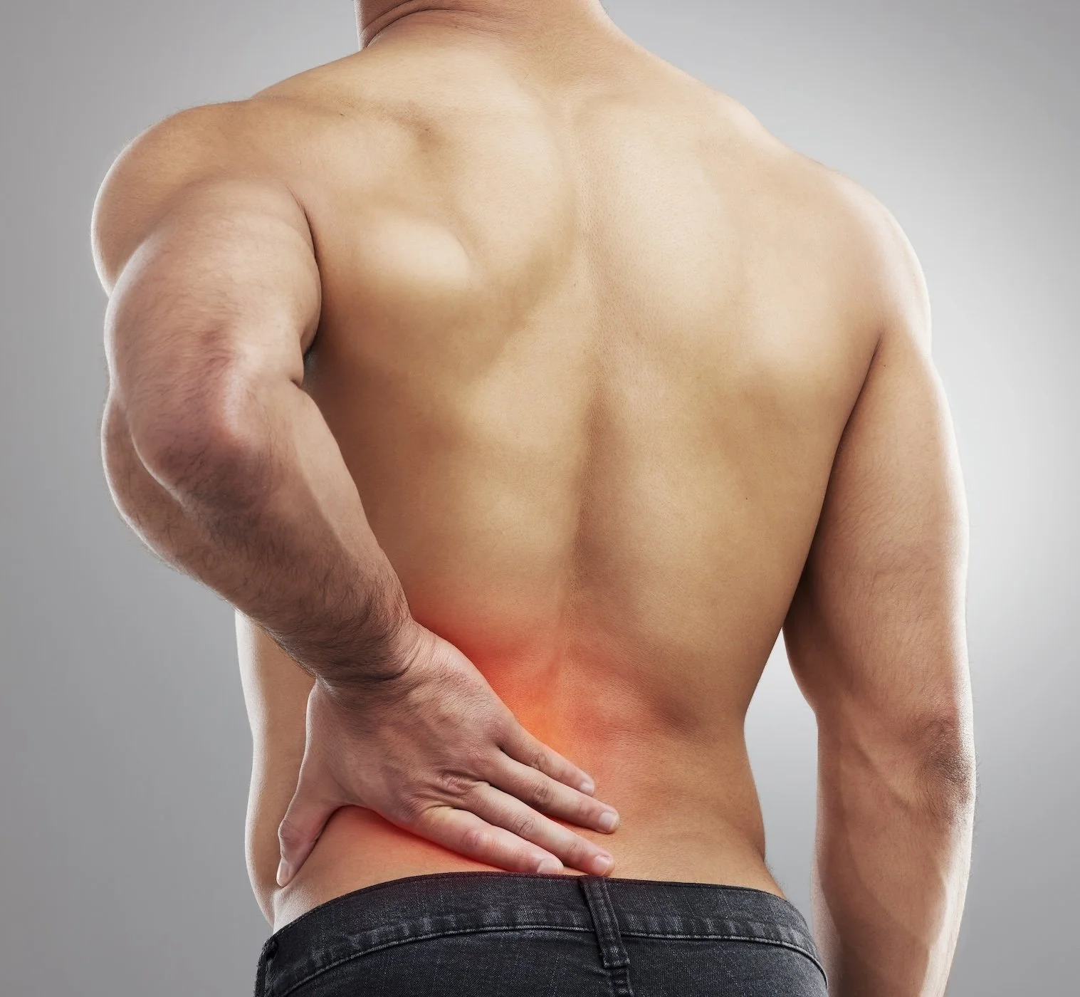 A shirtless man with one hand on his lower back, appearing to experience pain or discomfort in that area.